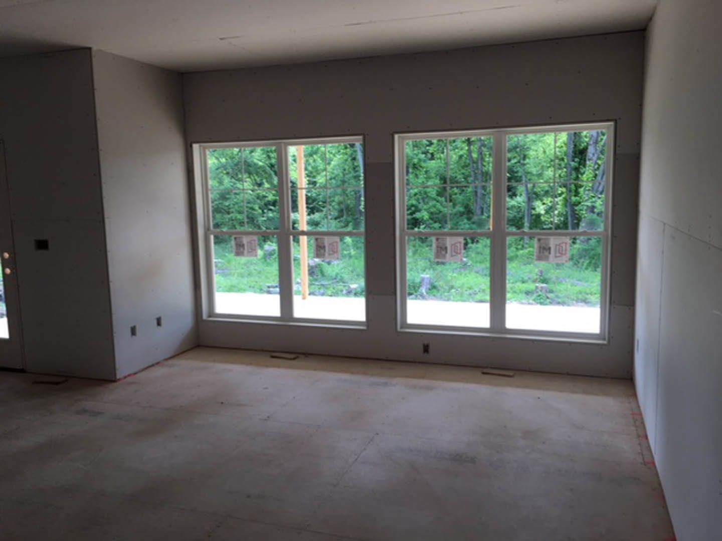 Spacious room featuring large windows, smooth concrete flooring, white walls, and views of green trees outside