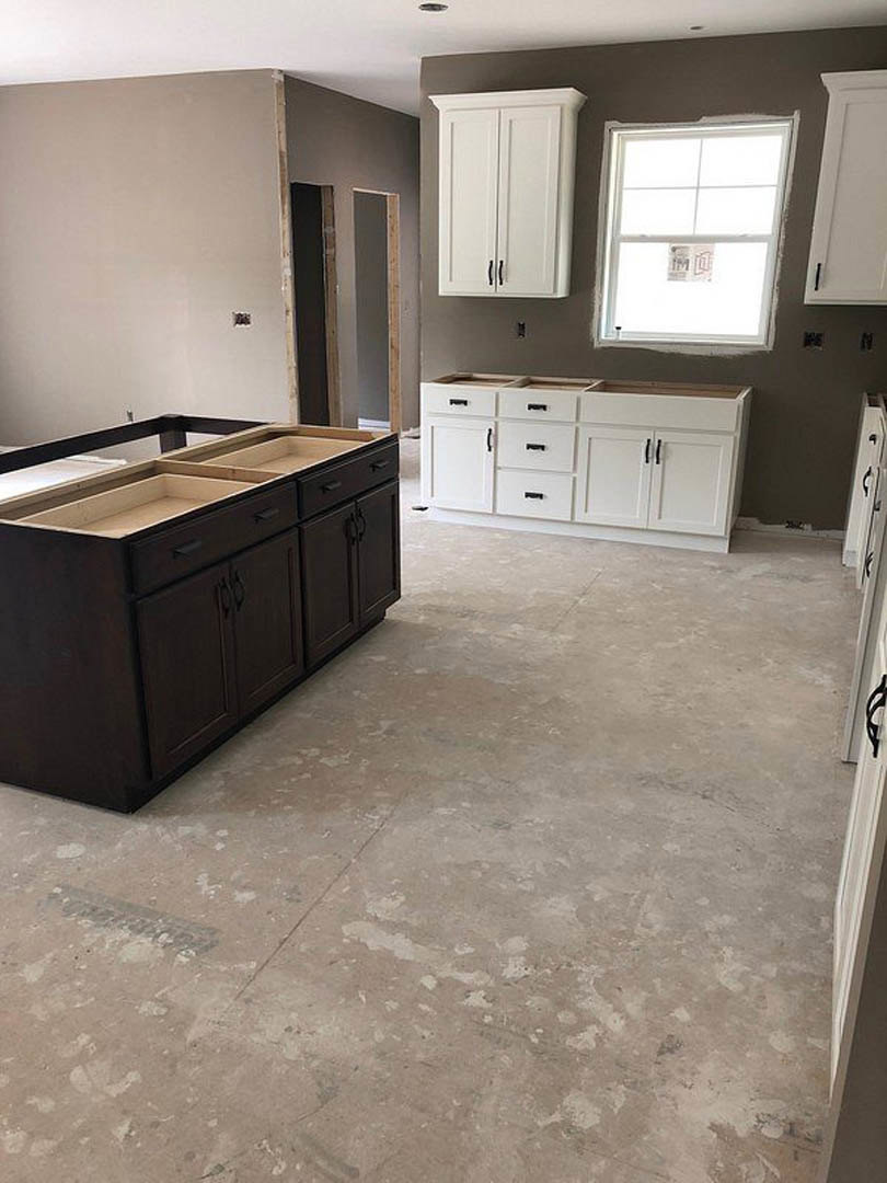 White kitchen cabinets with black handles, black countertop, stainless steel sink, tile backsplash, large window with a sign, light-colored flooring