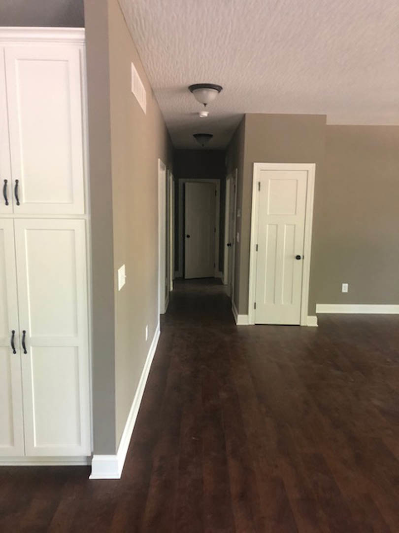 Hallway with dark hardwood floors, white doors featuring black knobs, white cabinet with black handles, white trim, and wall-mounted light fixture