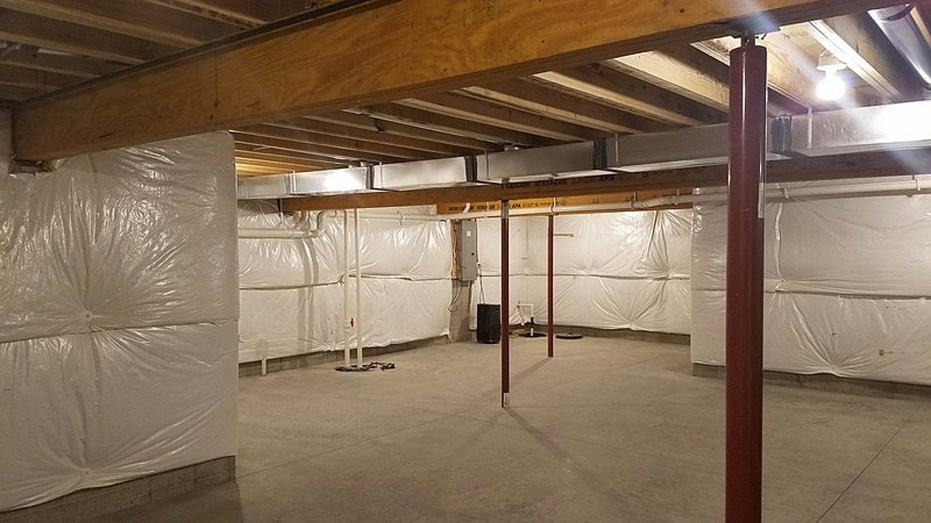 Room under construction with white plastic sheeting covering walls and floor, exposed ceiling beams, plaster surfaces, and scattered construction materials.