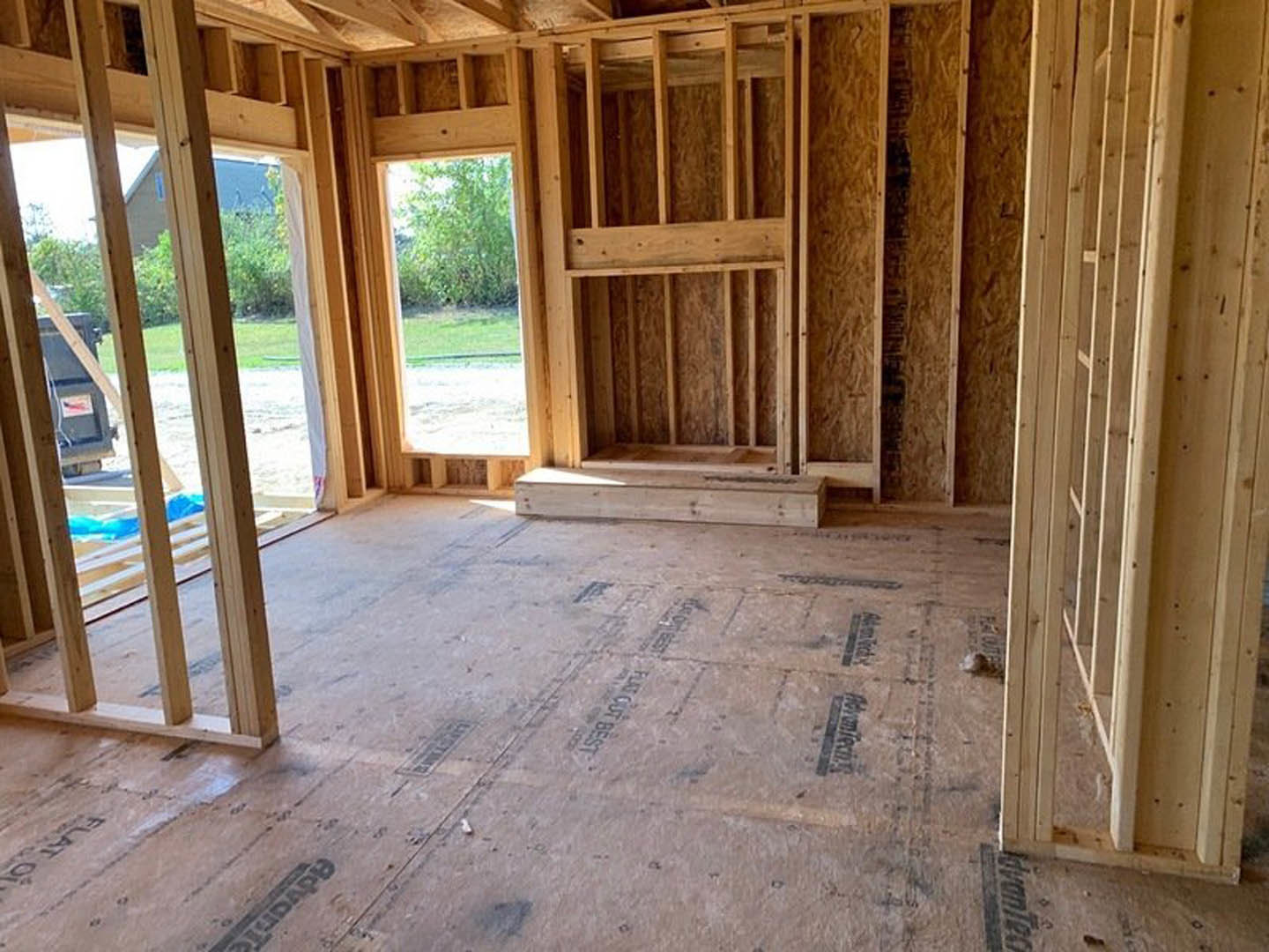 Wood-framed room under construction with exposed beams, unfinished hardwood flooring, and a framed window opening.