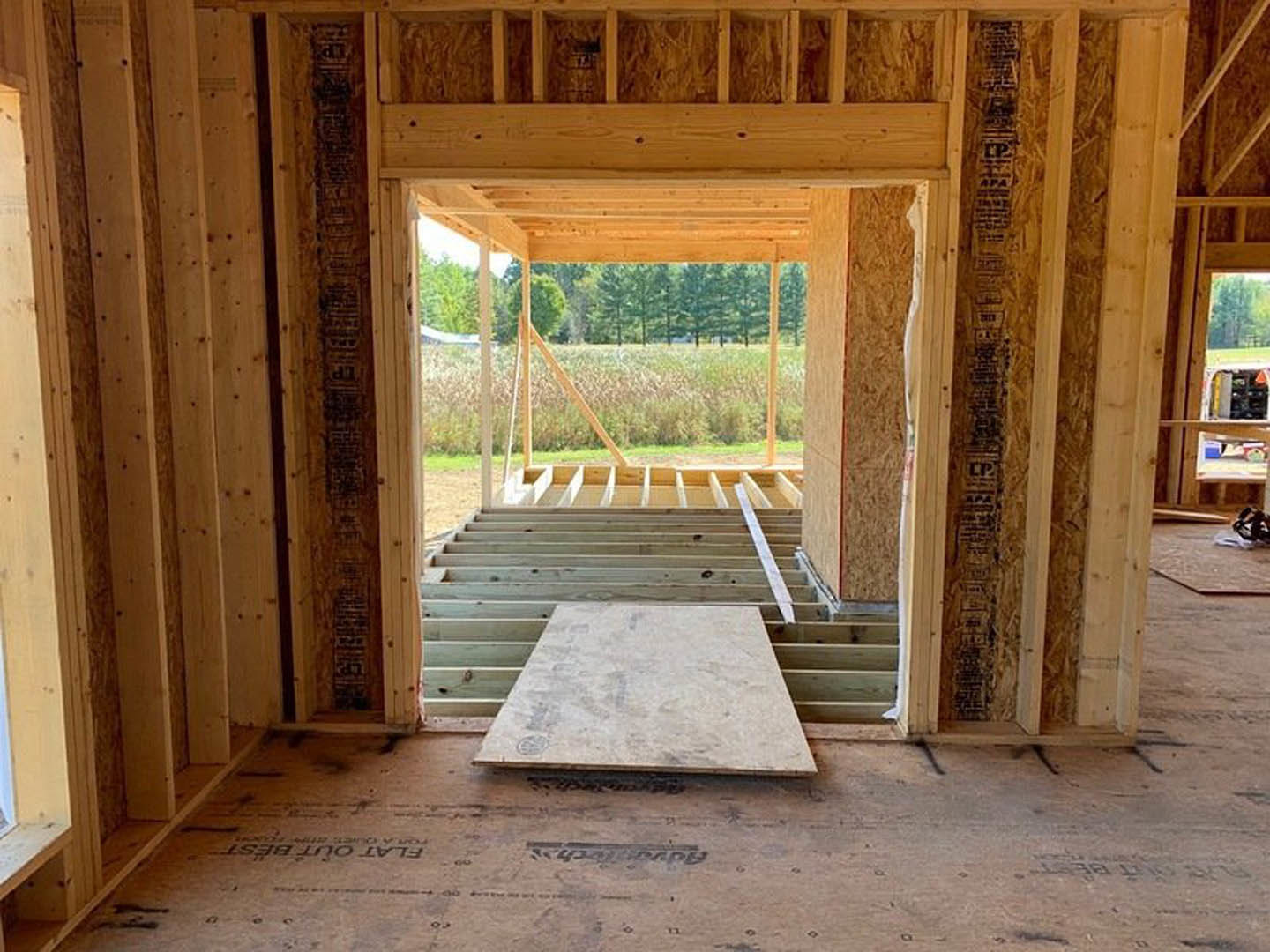 Wood-framed room under construction with exposed beams, open doorway, and unfinished wooden floor
