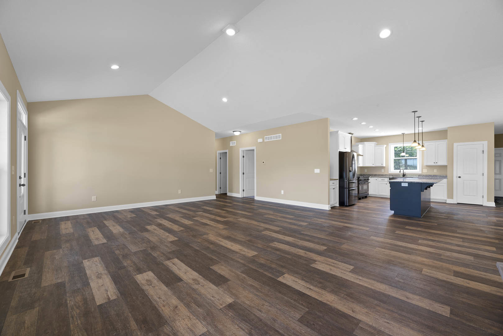 Spacious open floor plan featuring hardwood flooring, modern kitchen with white cabinetry and stainless steel refrigerator, kitchen island, white ceiling with recessed lighting