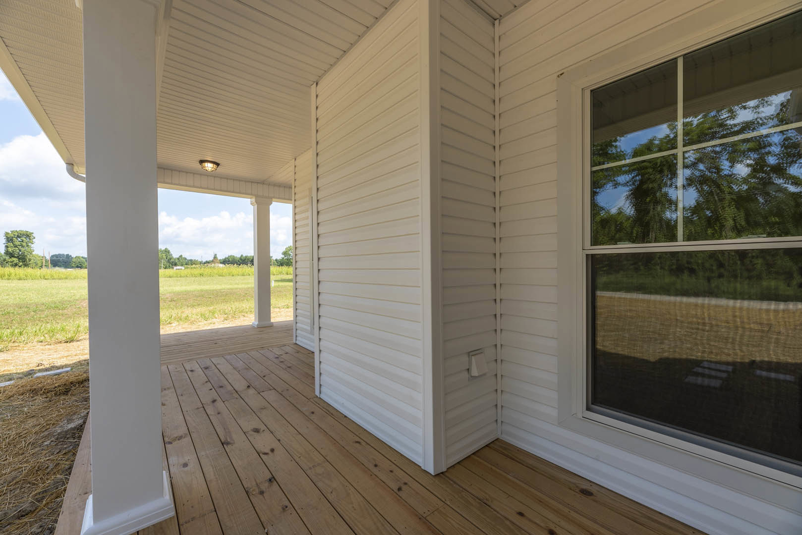 White siding house with large windows, wooden deck, grassy yard, leafy tree, and tree reflections visible in window glass