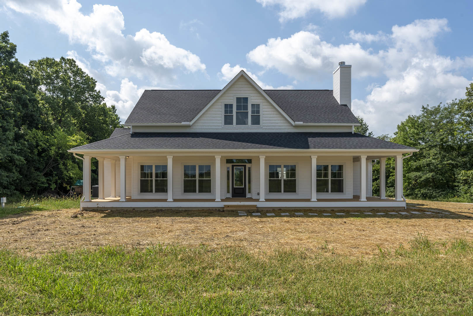 White custom home with covered porch, prominent columns, large windows, and expansive green lawn under partly cloudy sky