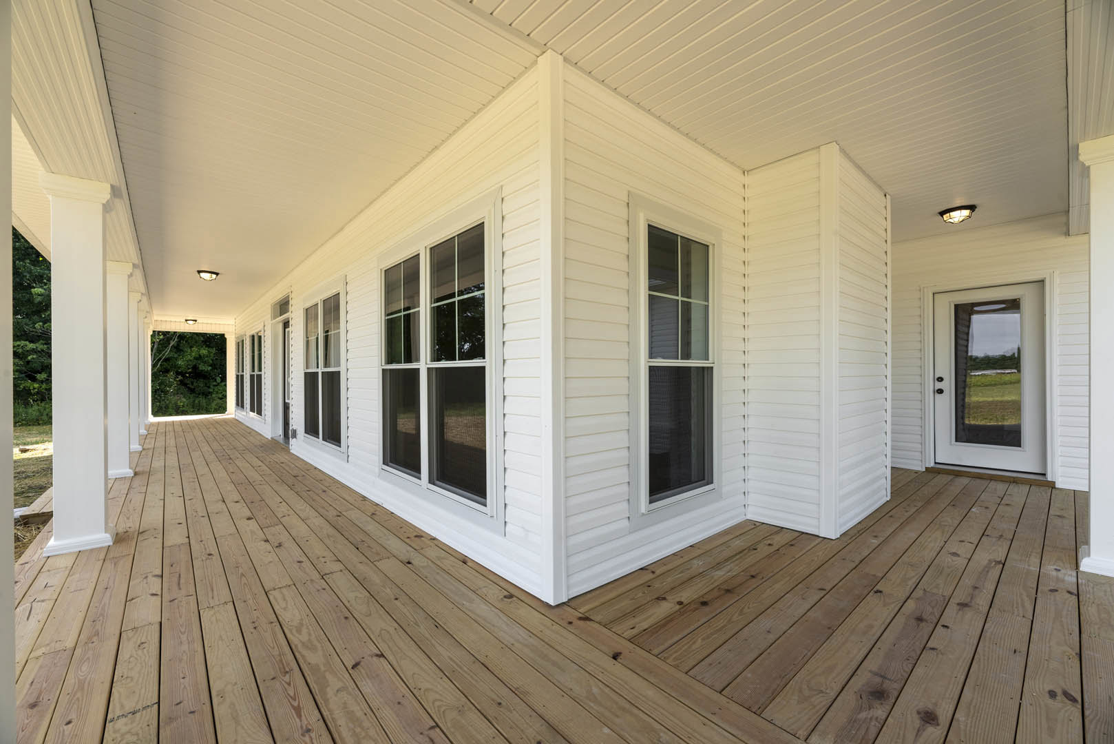 White exterior home with wood deck, glass door overlooking grassy field, close-up of white-framed window with black screen