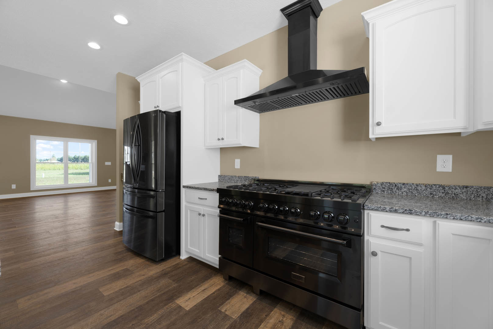 Black appliances and white cabinetry in a modern kitchen, including a black refrigerator and stove with glass door, open cabinet door, white outlet on the wall, and window