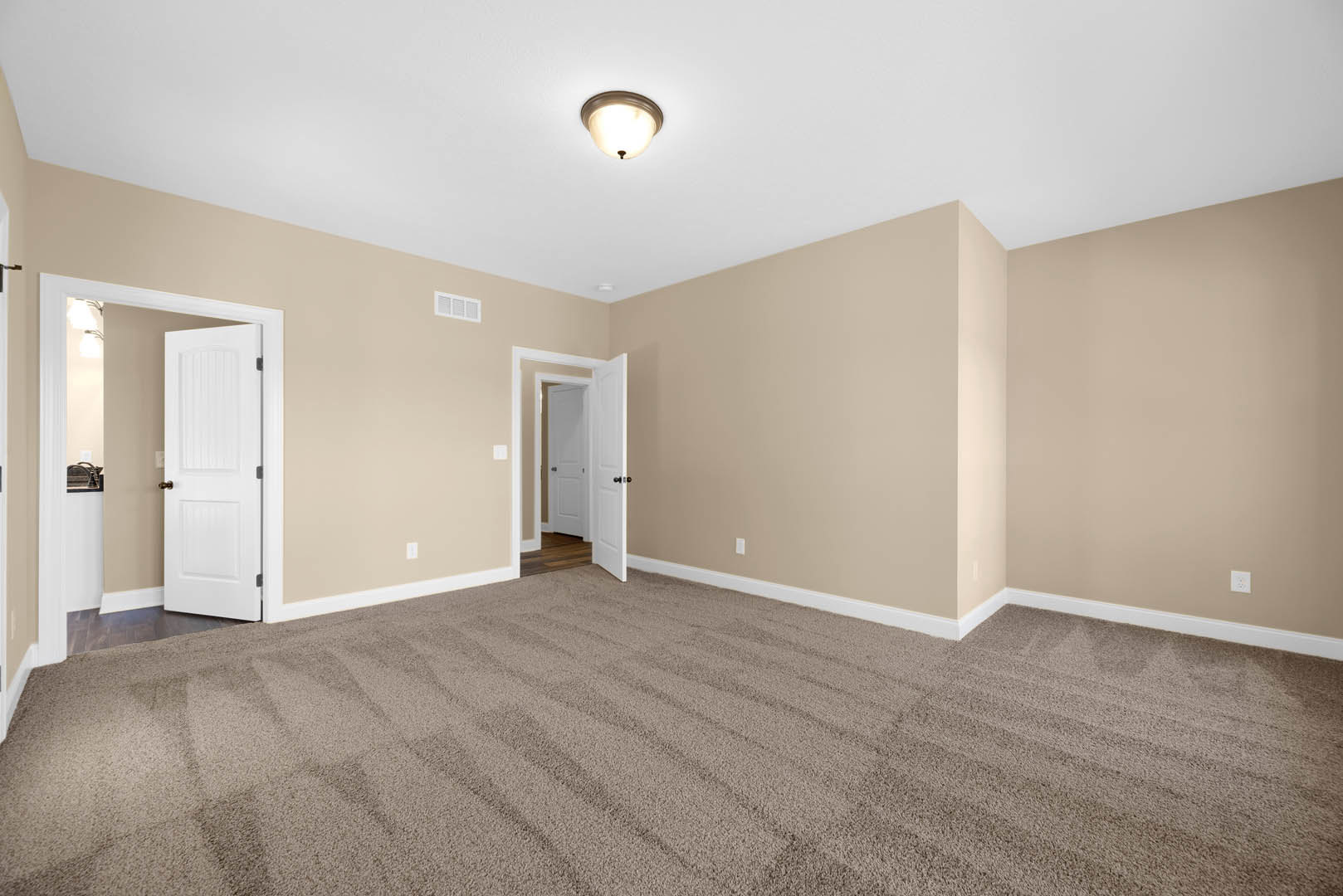 Beige walls and carpeted floor, white door with gold handle, ceiling-mounted light fixture