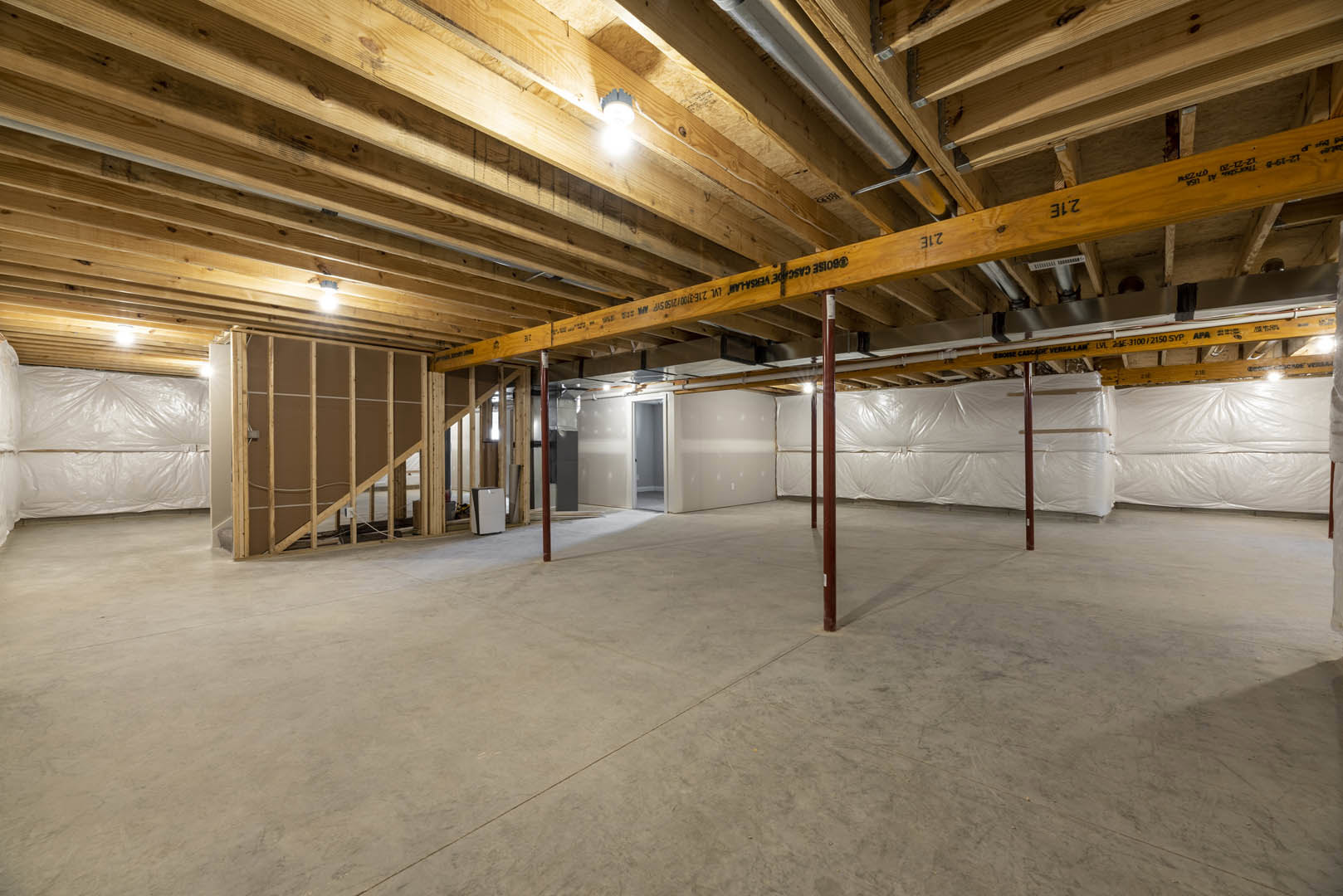 Open room with exposed wooden ceiling beams, concrete floor featuring a central line, wall-mounted white rectangular object with black border, ceiling light fixture, and white