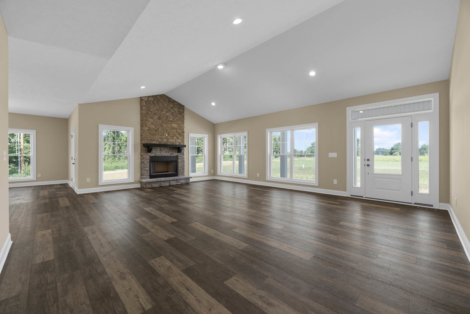 Spacious living area with hardwood floors, black-framed fireplace, large windows overlooking forest and field, and white glass-paneled door