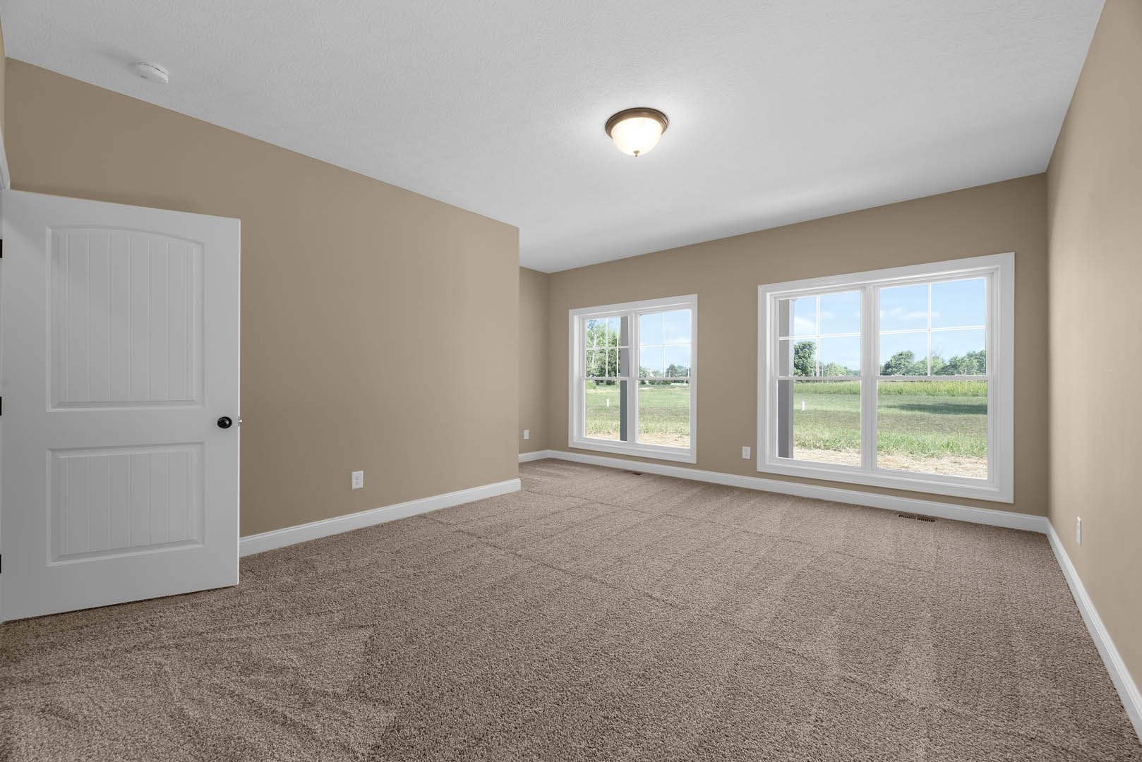 Carpeted room featuring a white door with black knobs, large window overlooking a grassy field, light fixture on white ceiling, and neutral plaster walls.