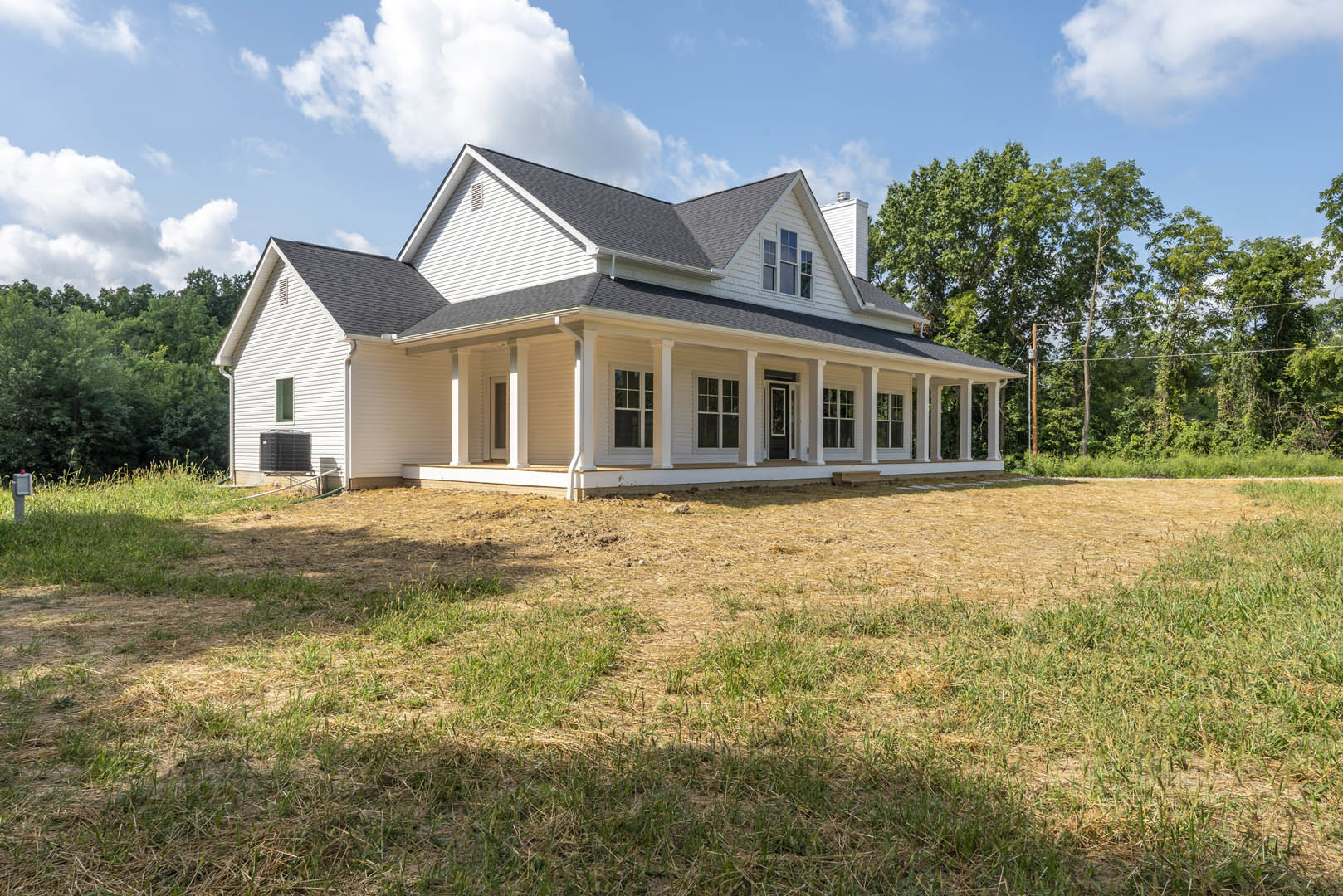 White custom home with multi-pane windows, covered porch, and dark roof, set on expansive green lawn under blue sky with scattered clouds