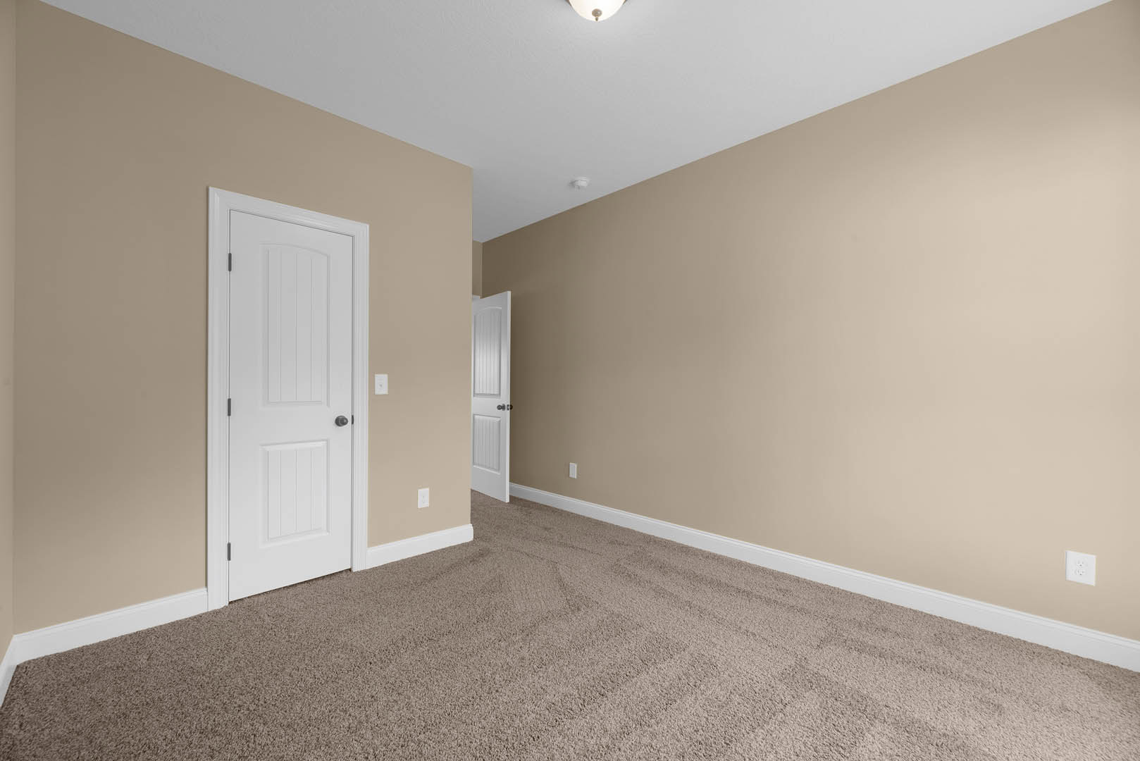 Beige-walled room with white paneled doors featuring black knobs, white electrical outlet, light-colored carpet, white door with blinds, and white ceiling with recessed light