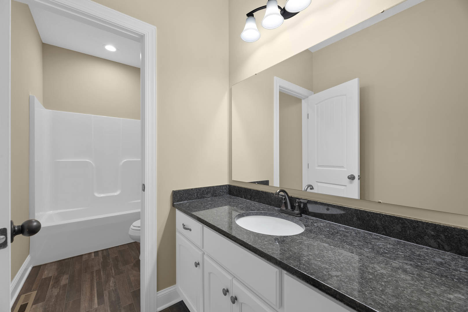 Modern bathroom featuring a white vanity with integrated sink, rectangular mirror above, black faucet and hardware, white bathtub with black handle, light fixture mounted on tile