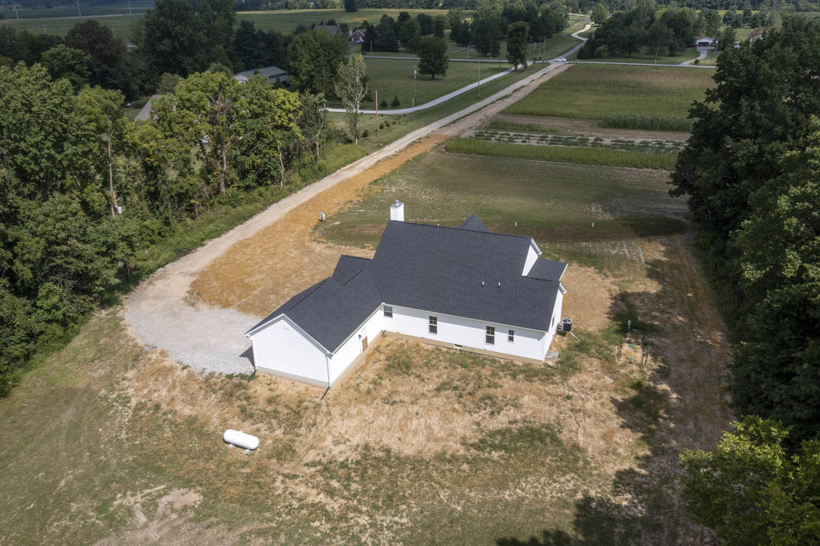 White house with black roof surrounded by green grass, trees, and a paved road in a rural landscape