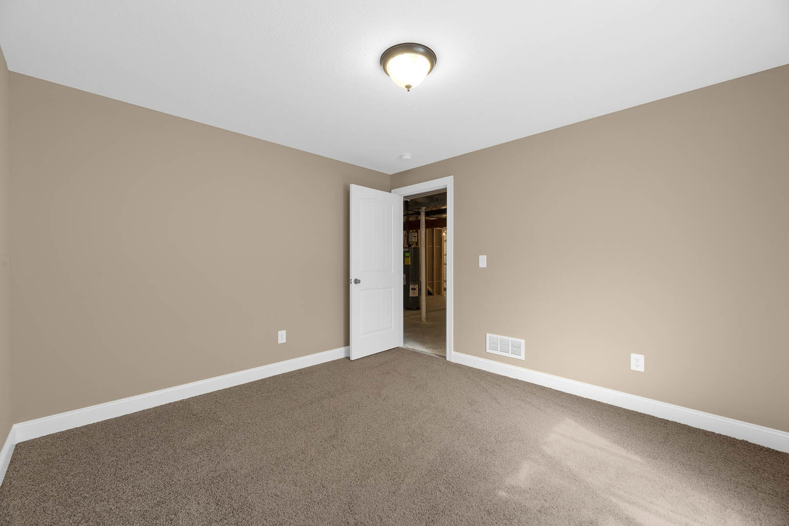 White paneled door with silver knob open to carpeted room, white wall vent, ceiling light fixture, and crisp white trim molding
