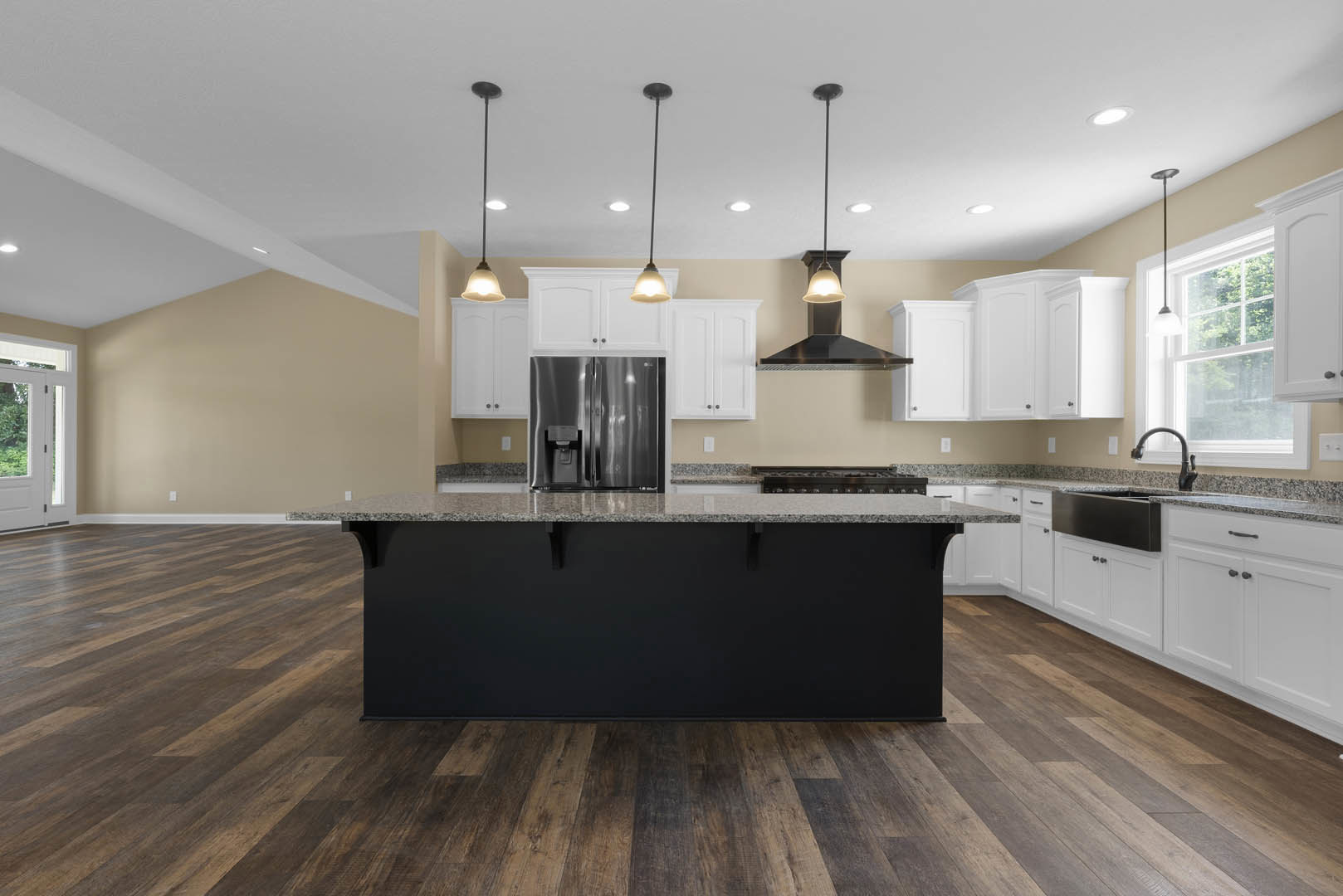 Spacious kitchen featuring a large marble-topped island, black countertops, wood flooring, stainless steel refrigerator, modern light fixture, and white cabinetry.
