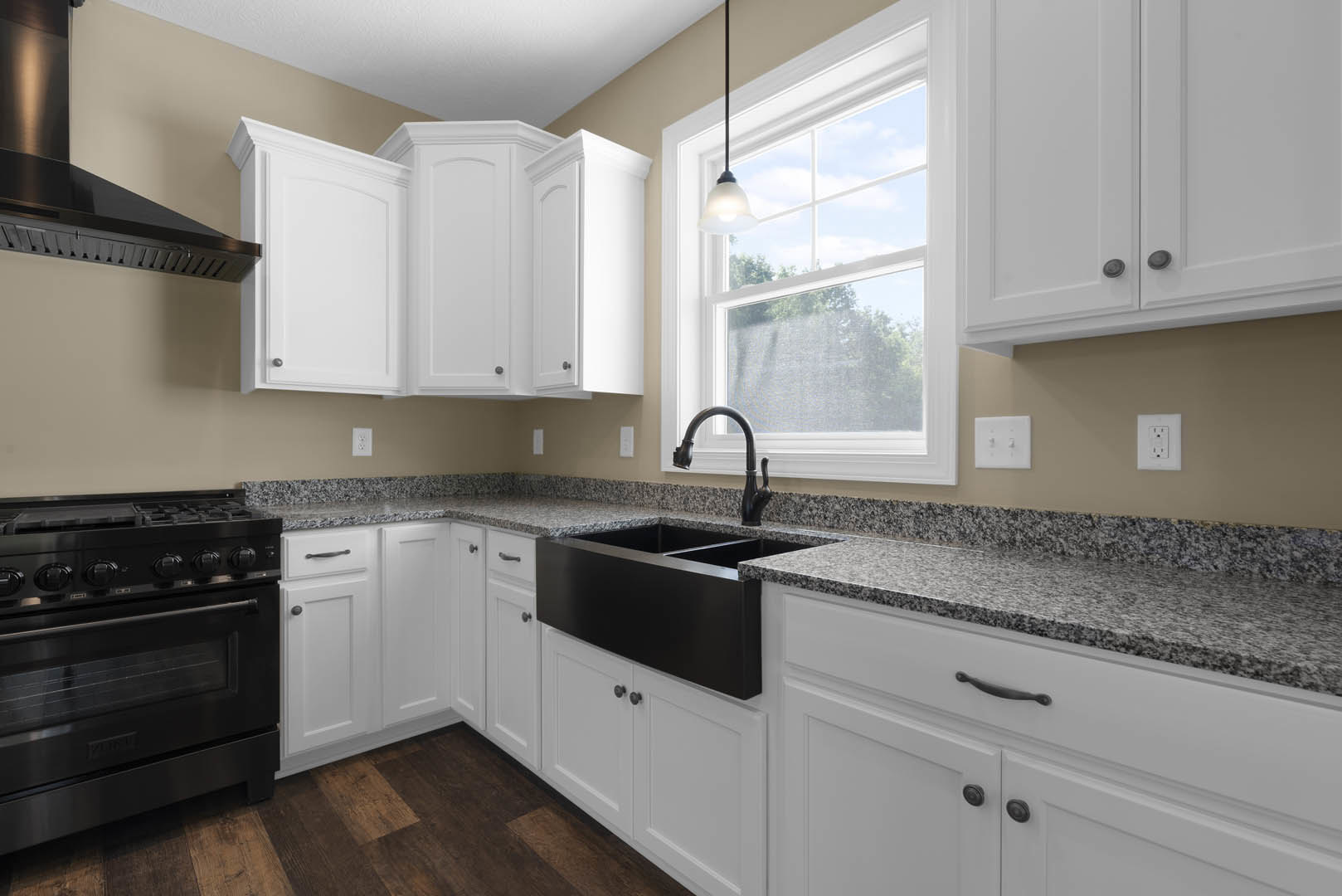 White kitchen cabinets, black undermount sink with matching faucet, granite countertops, stainless steel stove, white wall outlet, recessed ceiling light, black pole with white