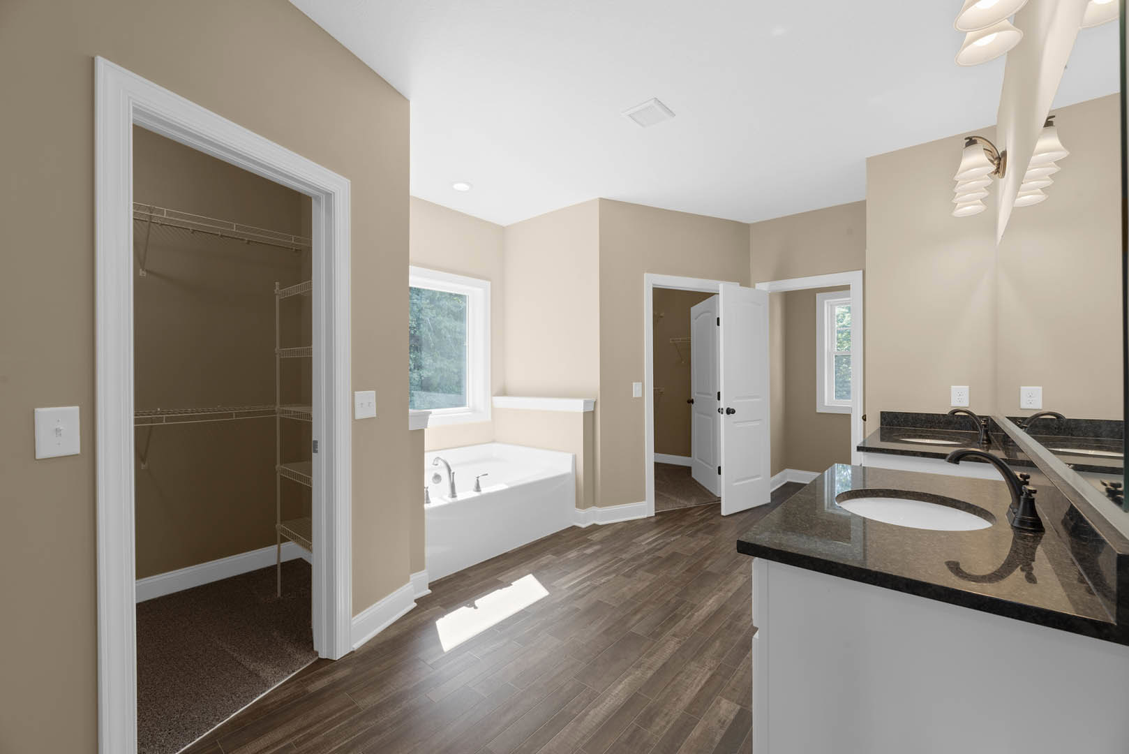 Bathroom with freestanding bathtub and rectangular sink, white tile floor, shadow cast across tiles, light switch on wall, window with white frame, white door with black knobs