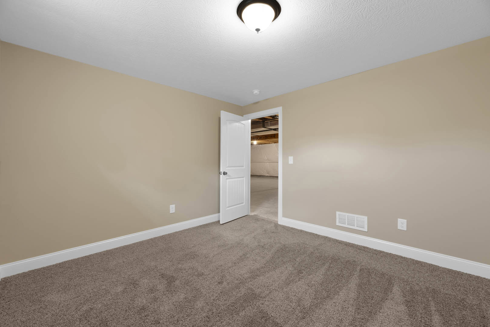 White paneled door with silver knob open to carpeted room, white wall vent, ceiling light fixture, and crown molding visible