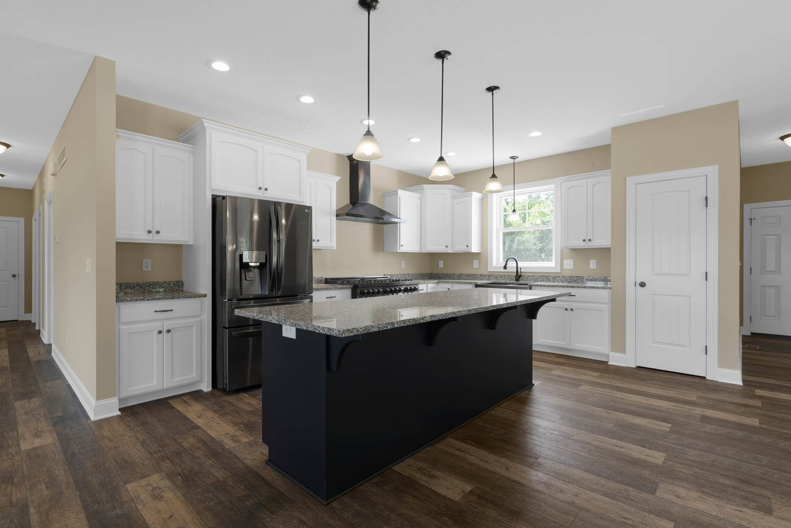 Spacious kitchen featuring a large granite island, stainless steel refrigerator with ice maker, white cabinetry, square panel white door with black handle, and black pole light
