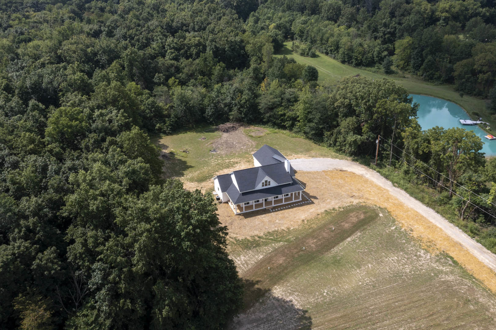 Two-story custom home with large wraparound porch, nestled among mature trees, surrounded by lush grass and dense forest