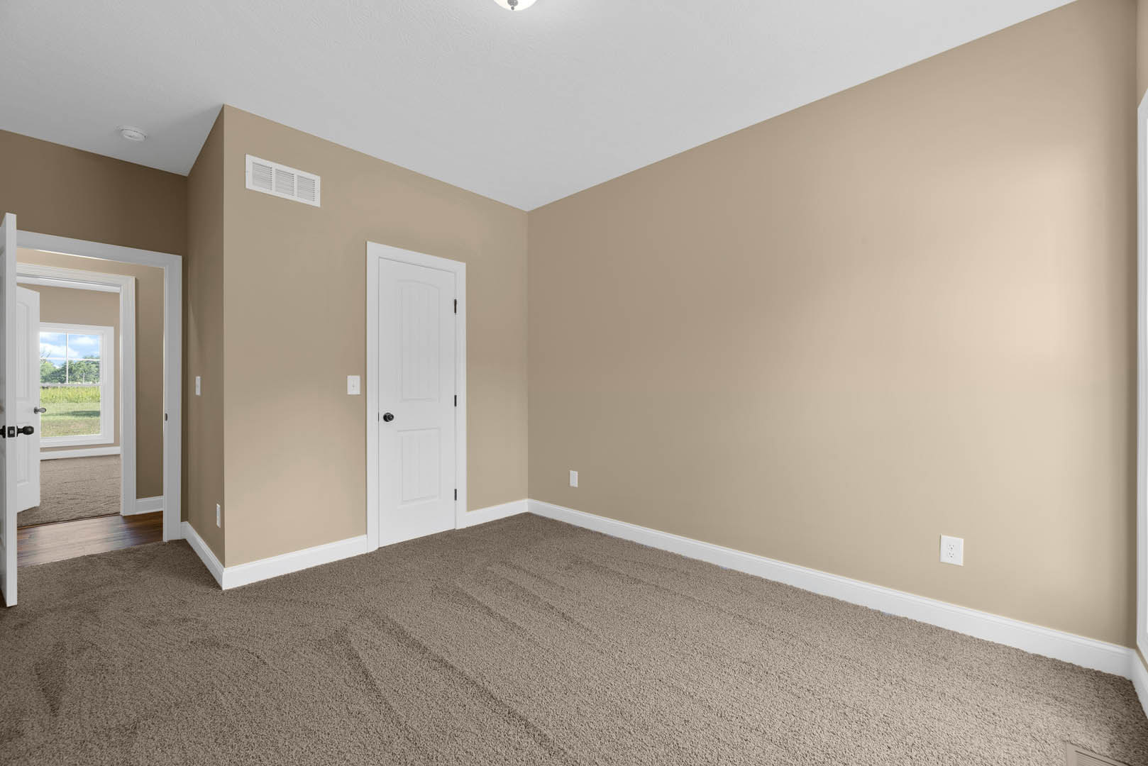 Beige-walled room with white door featuring black knob, carpeted floor, wall vent, and door opening to grassy field