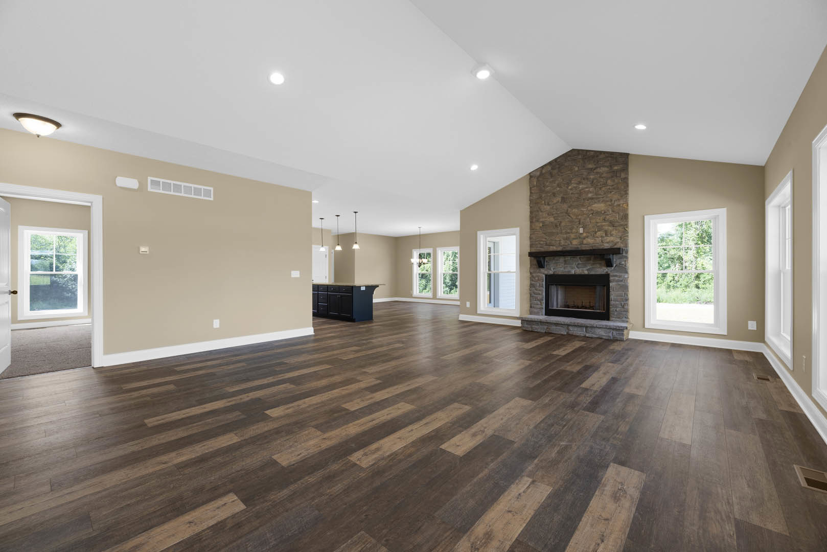 Spacious living room featuring hardwood floors, central fireplace with white mantel, large windows overlooking leafy trees, black built-in cabinet with drawers, white walls, and