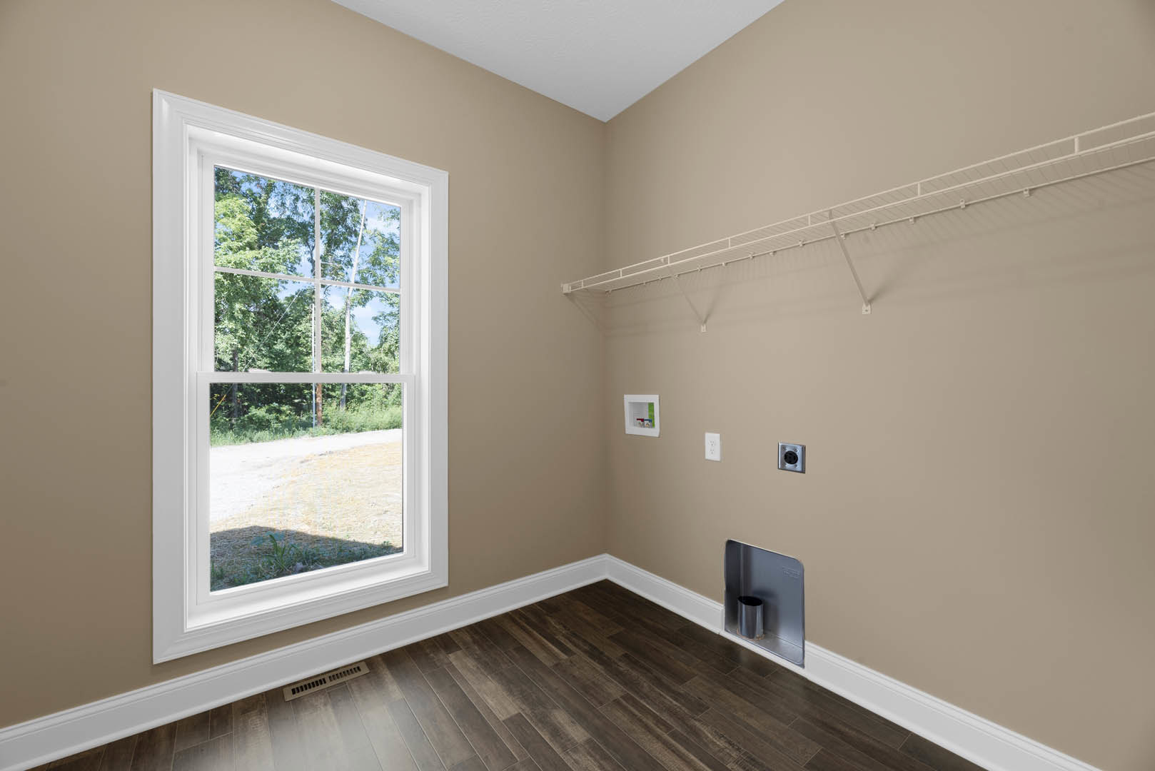Wood floor with white baseboard, white shelf with hooks mounted on plaster wall, square window with white trim overlooking trees, metal trash can recessed in wall.