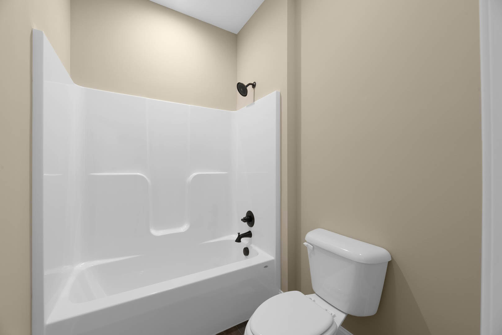 White bathtub and toilet with chrome faucet, wall-mounted shower head, and light-colored tile walls in a modern bathroom.