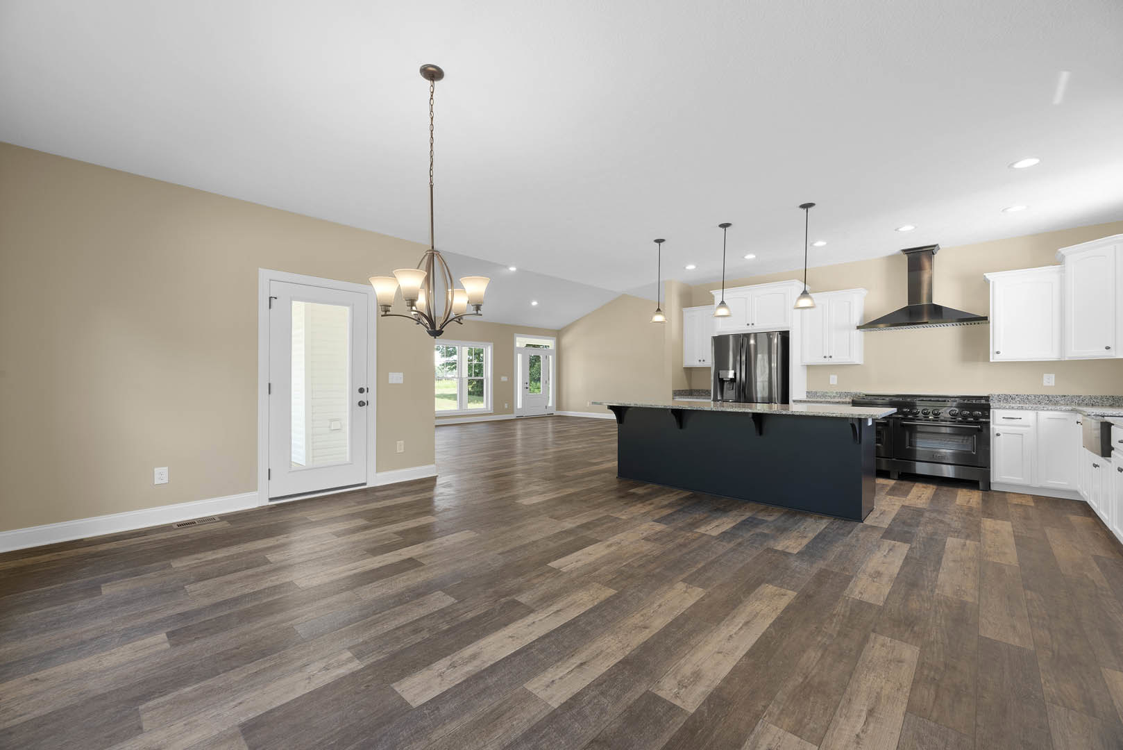 Open-concept kitchen and living room with hardwood flooring, white door and pillar, black marble-topped counter, stainless steel refrigerator with dispenser, black oven with knobs