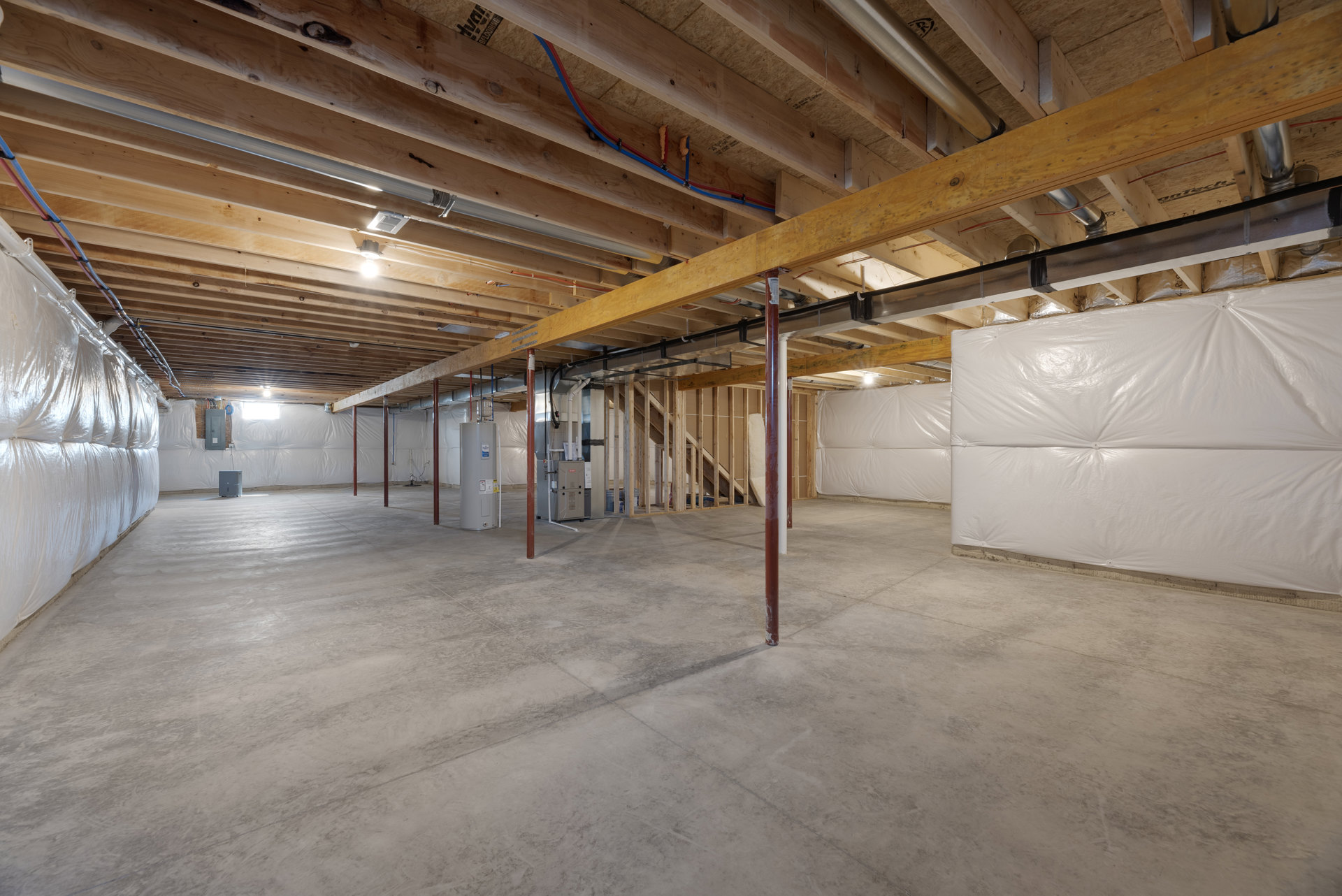 Concrete floor with exposed wooden ceiling beams, metal support pole, large white plastic-wrapped bag, and white plastic sheeting covering part of the wall