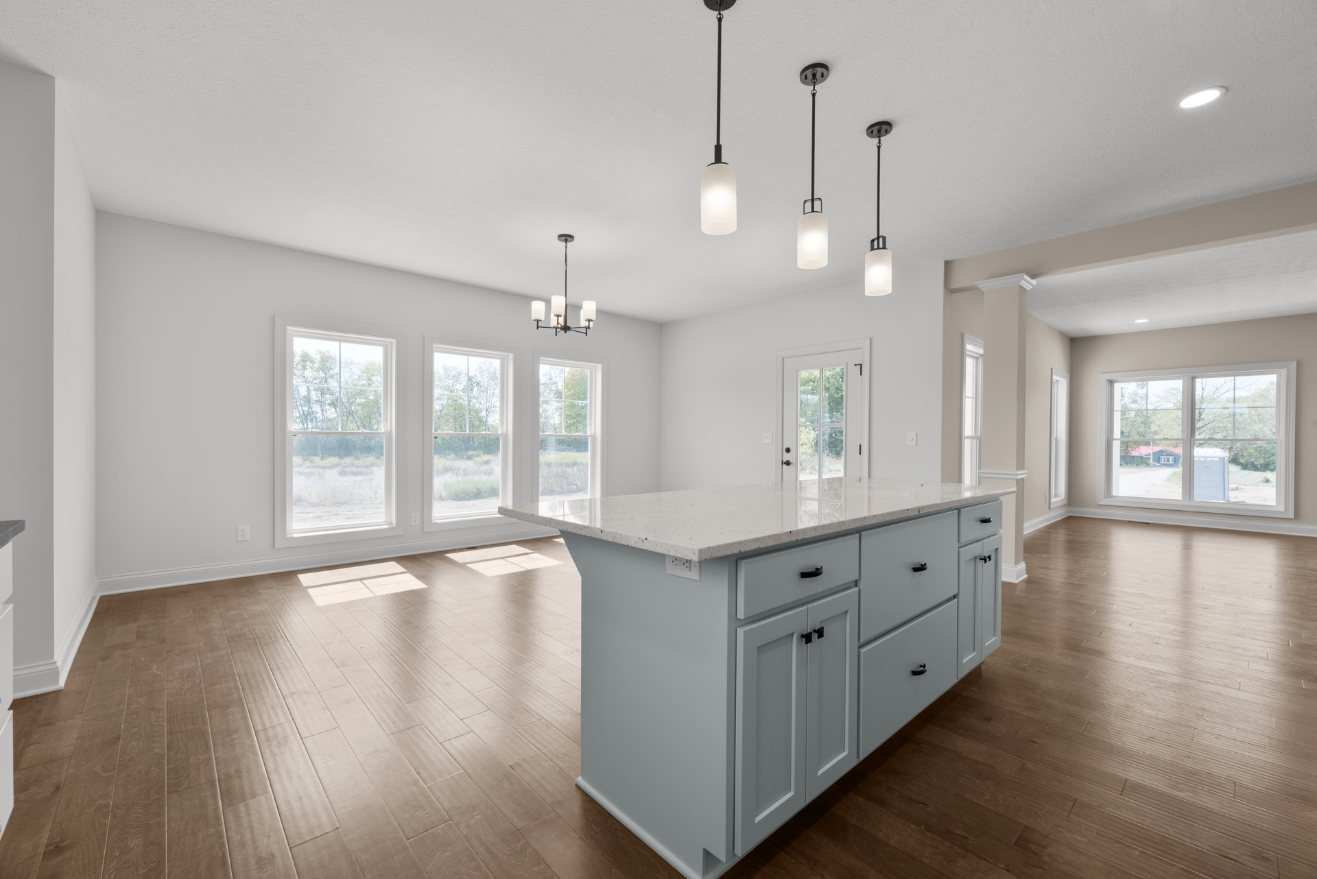 Spacious kitchen featuring a white island with black handles, white cabinetry, laminate flooring, large window overlooking yard and trees, and ceiling light centered on a white