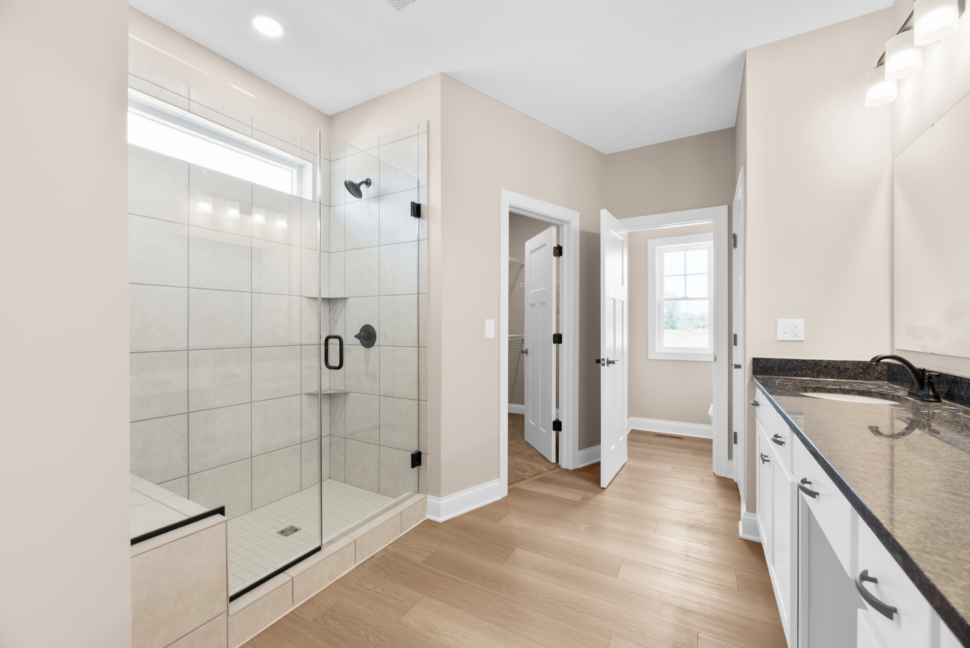 Bathroom featuring a glass-enclosed shower, white-framed window, tile flooring, and a vanity with a countertop sink and chrome faucet
