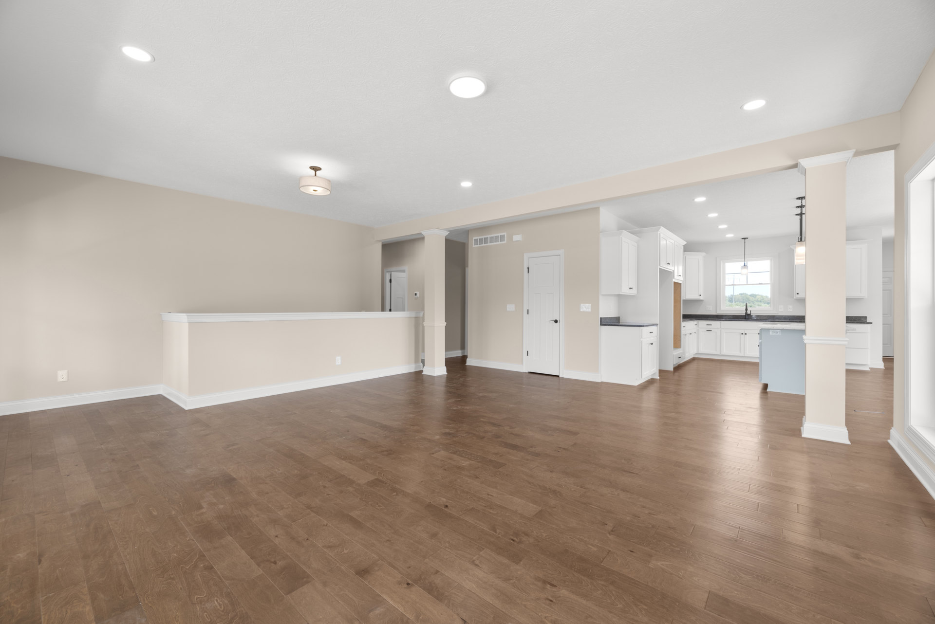 Spacious room with hardwood flooring, white walls, white cabinetry, black door handle, and ceiling-mounted light fixture with white shade