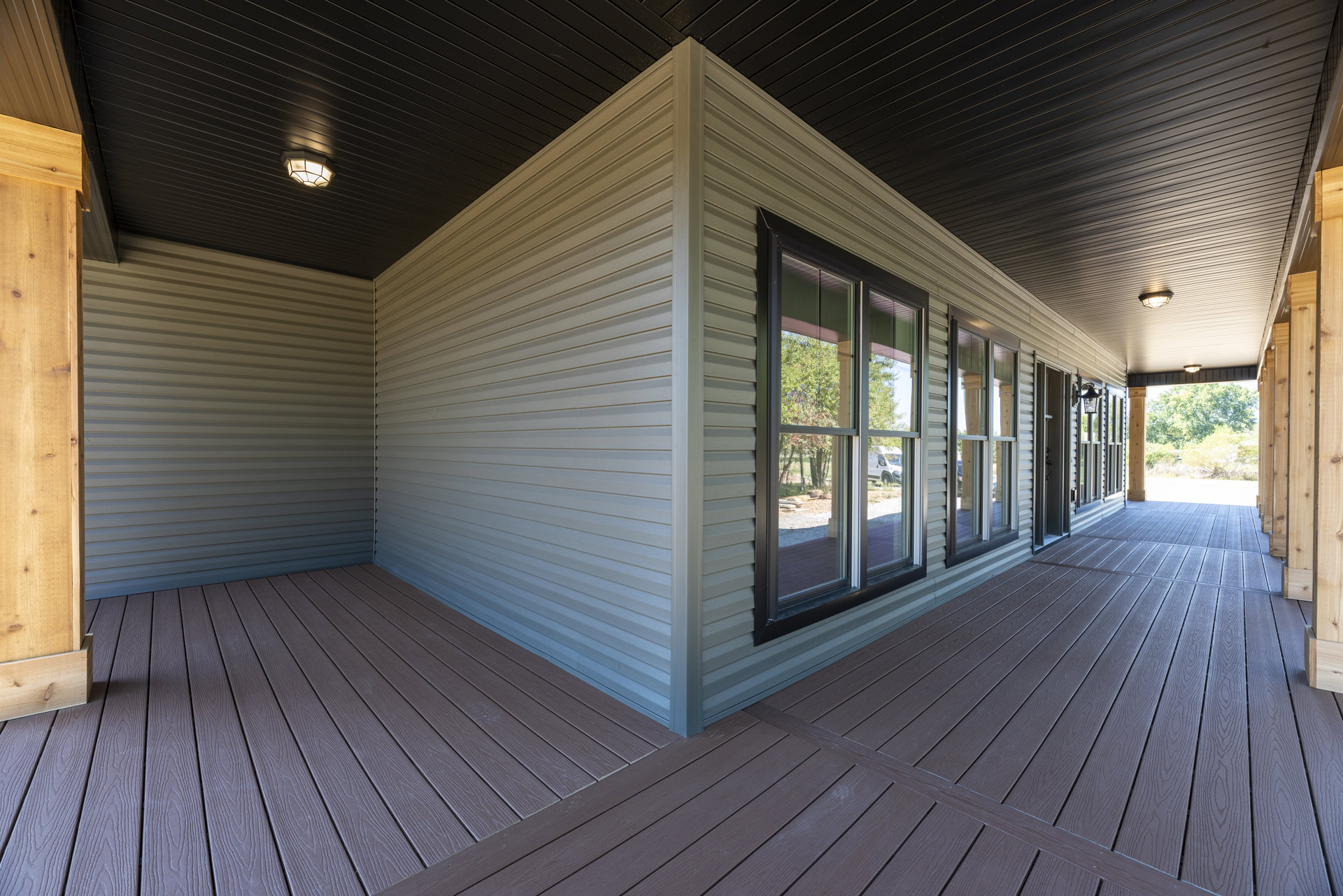 Wood deck with wide plank flooring, large window framed in wood paneling, view of trees and road through glass, row of windows along brick exterior wall