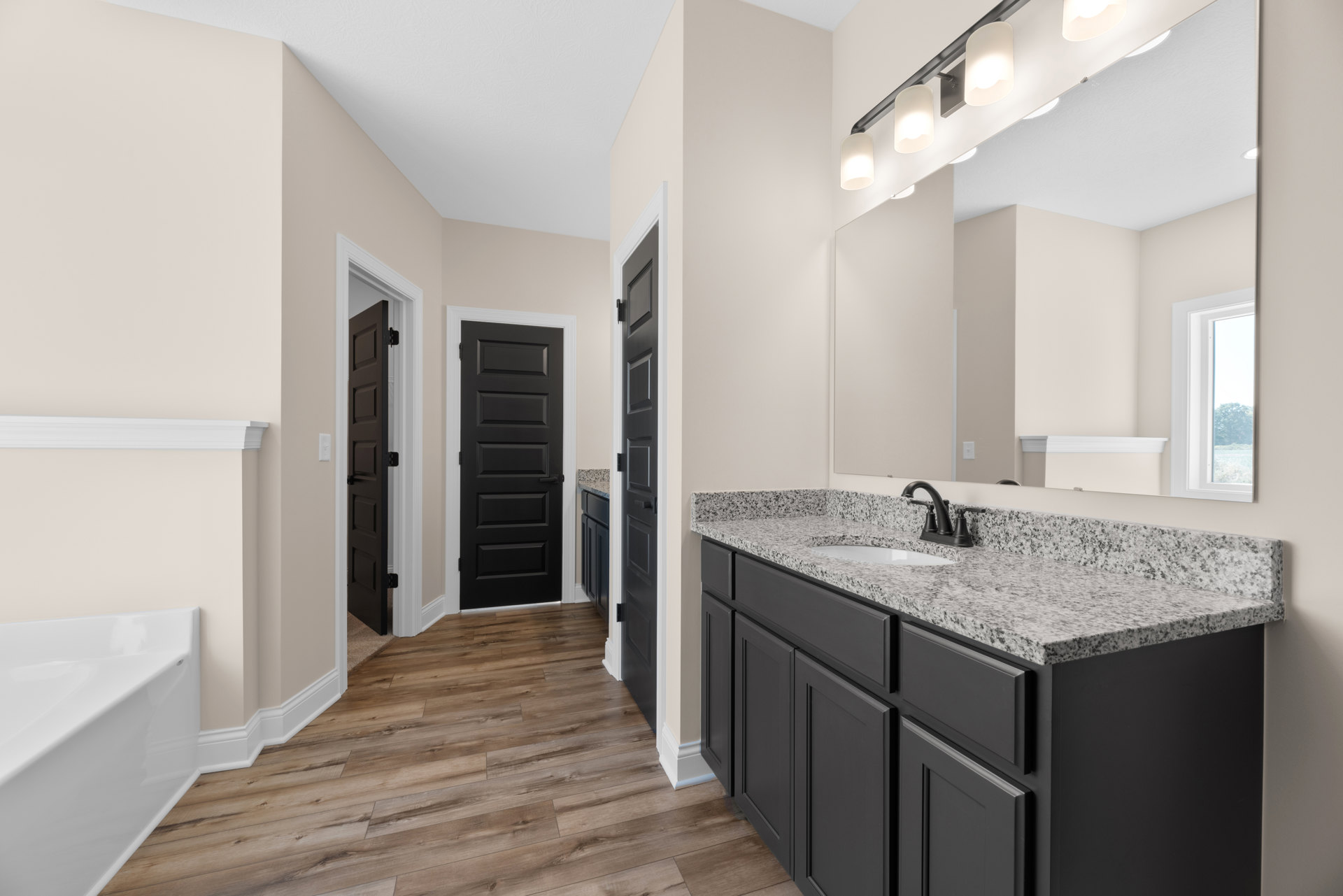 Bathroom featuring marble countertop, rectangular mirror, black faucet on white sink, white freestanding bathtub, wood flooring, black door with white trim, and modern light