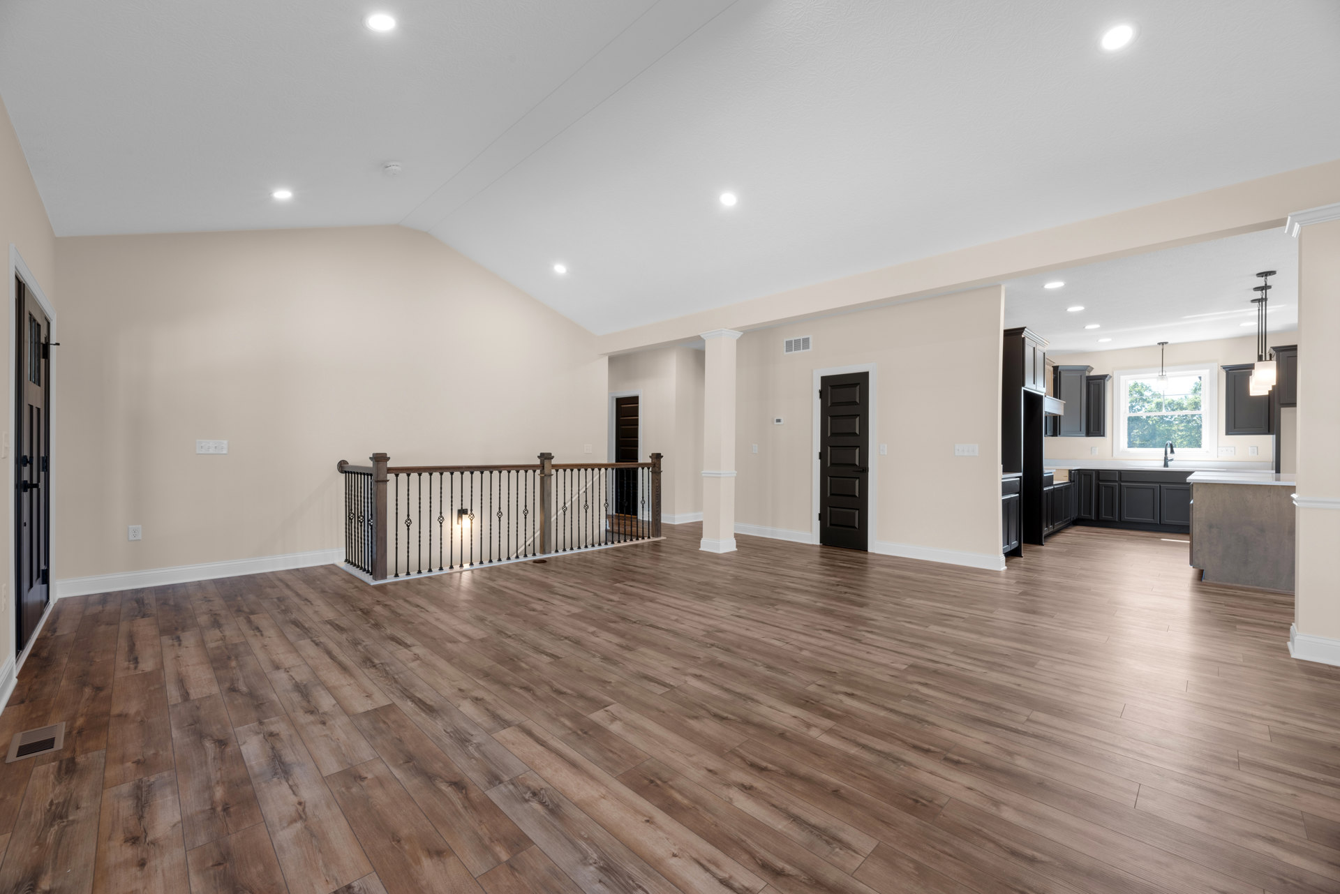 Spacious room with hardwood flooring, white walls, black door with metal handle, modern ceiling light, and wood railing