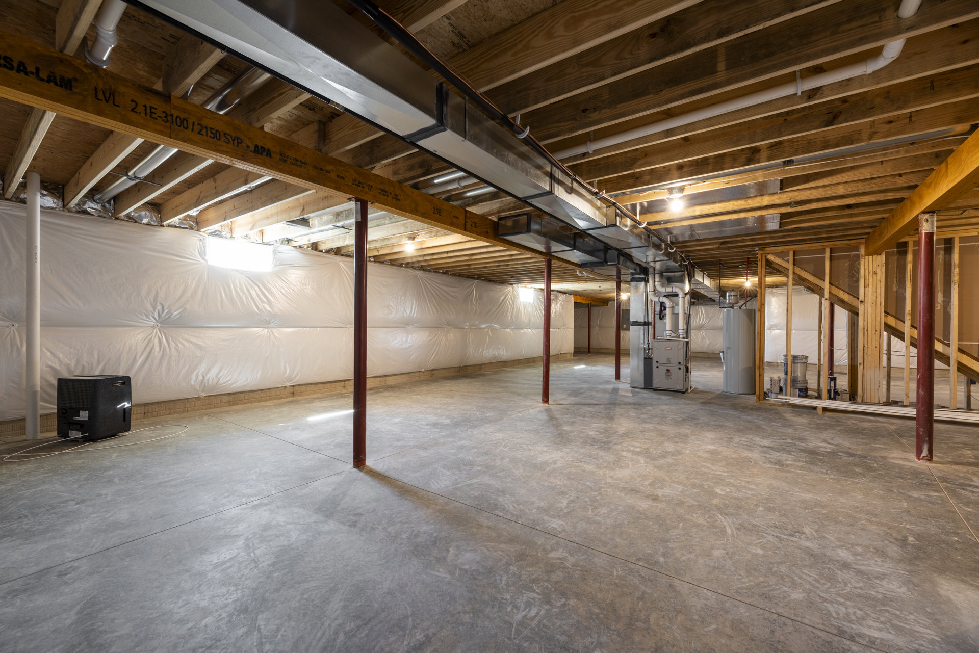 Spacious room with white walls, exposed wooden ceiling beams, concrete floor, and metal pipes running along the ceiling; red support poles and a white cabinet are visible.