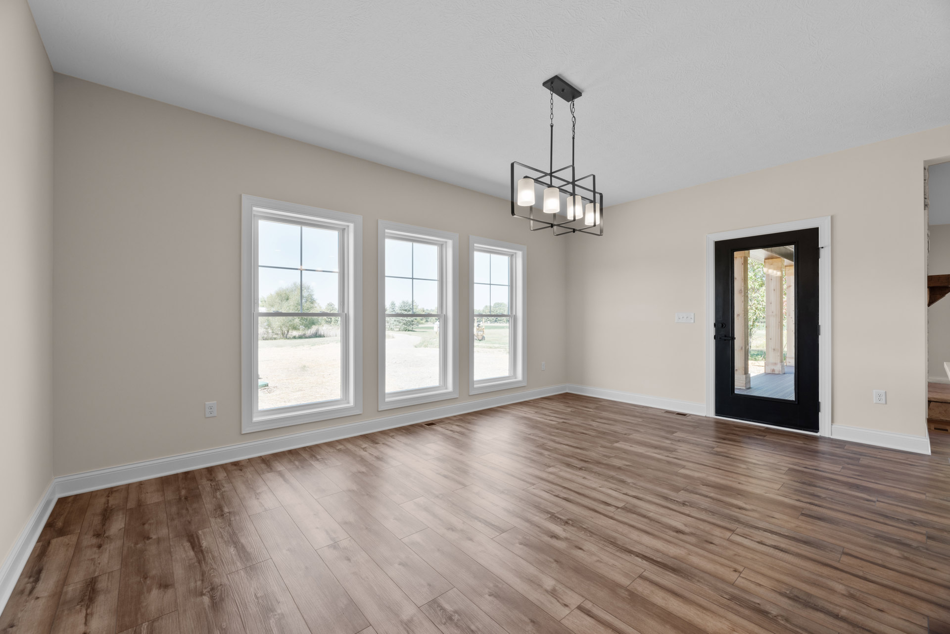 Room with hardwood flooring, black door, large windows overlooking trees and grass, plaster walls, and a modern chandelier.