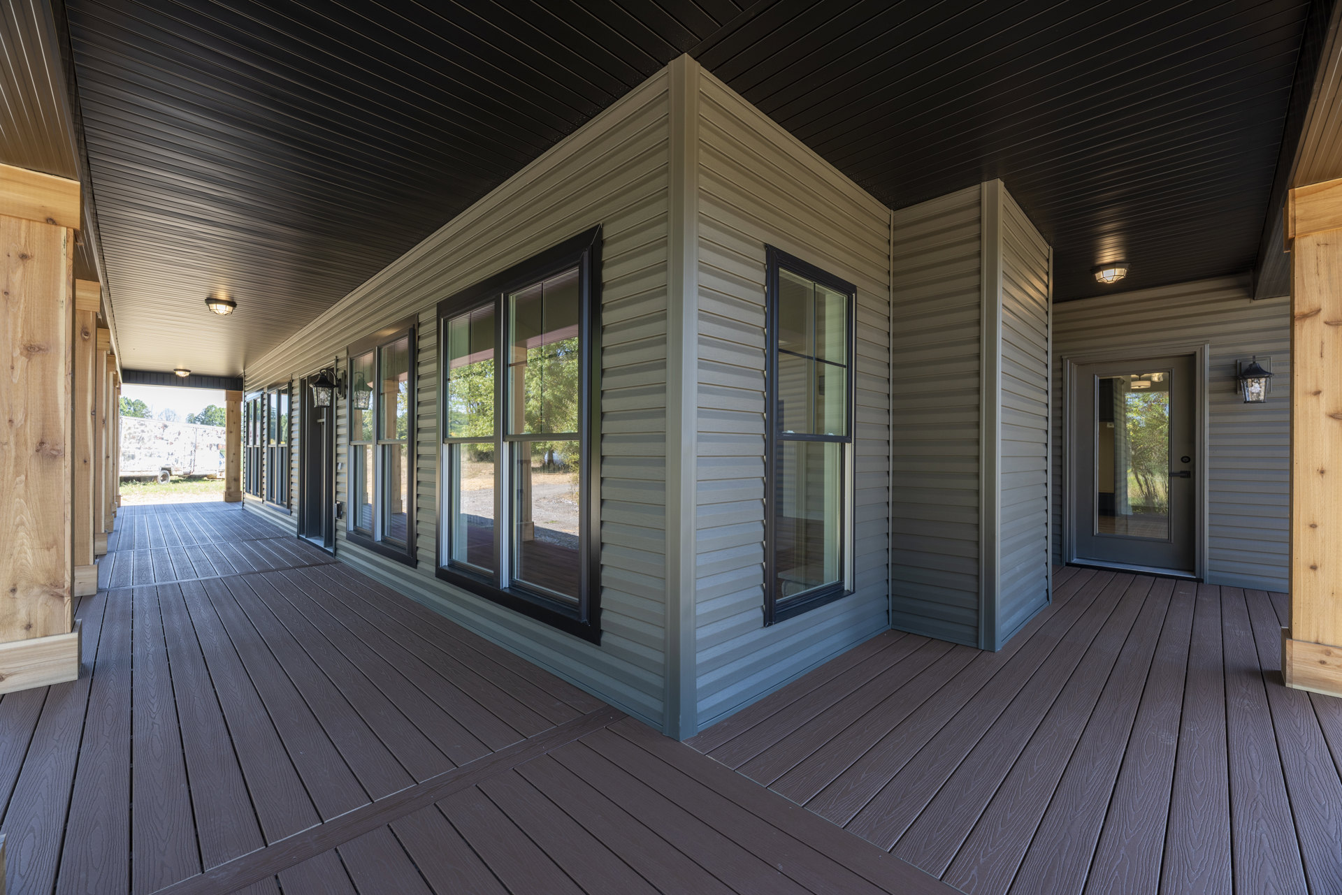 Modern home with wood deck, covered porch, large glass door, multiple windows, and trees visible outside