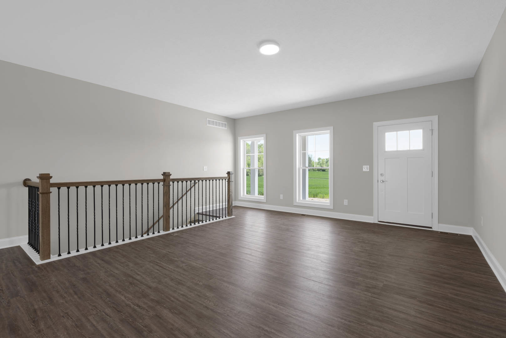 Wood flooring with a white door featuring a window, close-up of a hardwood railing, plaster walls, ceiling light fixture, and a window overlooking a green field