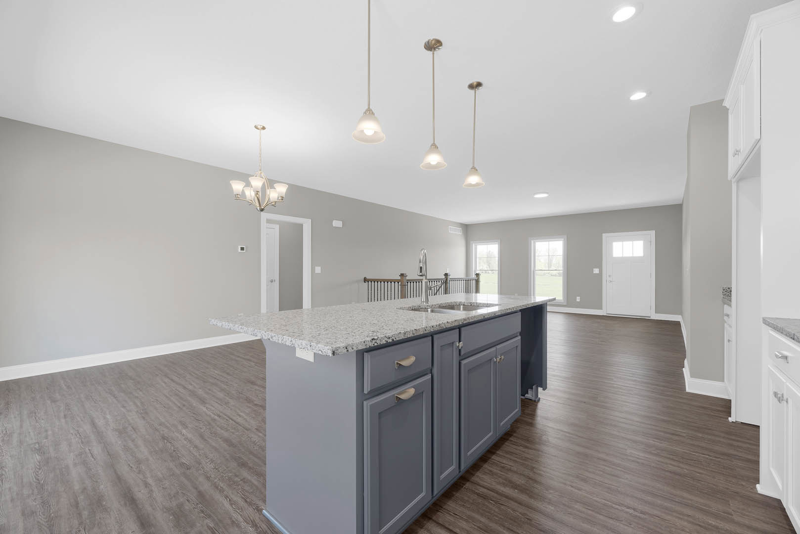 Granite kitchen island with built-in sink and drawers, white cabinetry, wood flooring, chandelier overhead, window and door offering view of grassy field.