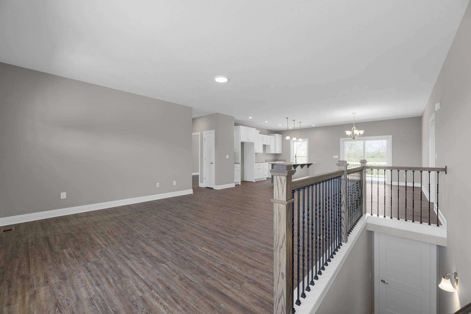 Wood flooring in a bright room with a modern metal railing, white door with silver handle, and decorative chandelier and wall light fixture.
