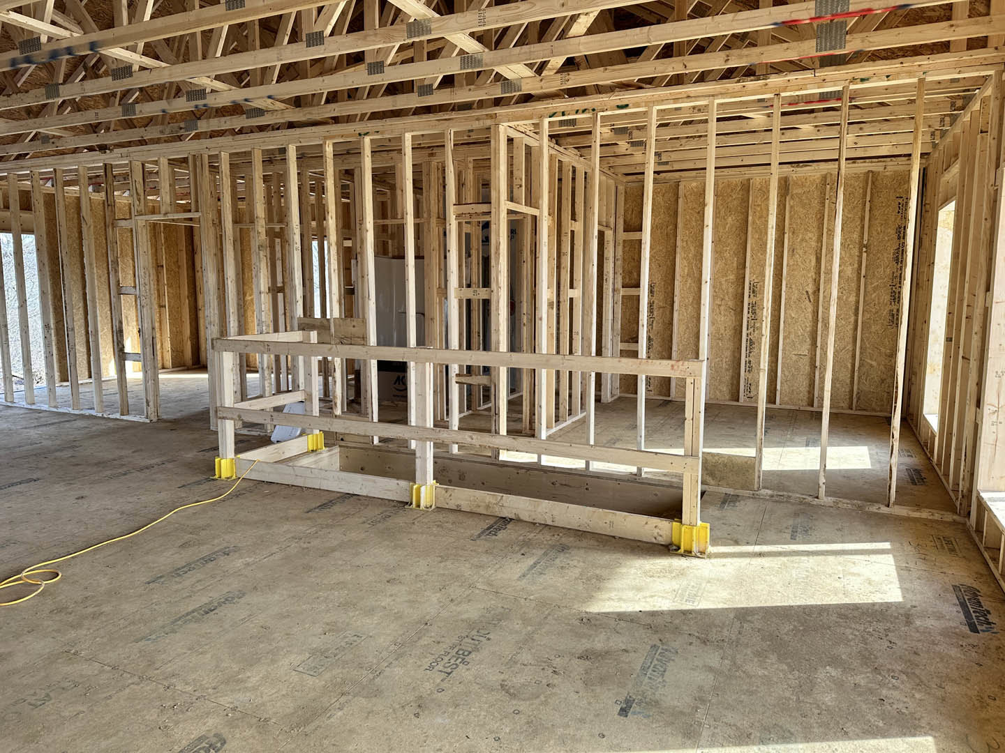 Exposed wood beams and framing with a concrete floor, yellow electrical cable on the ground, unfinished interior construction