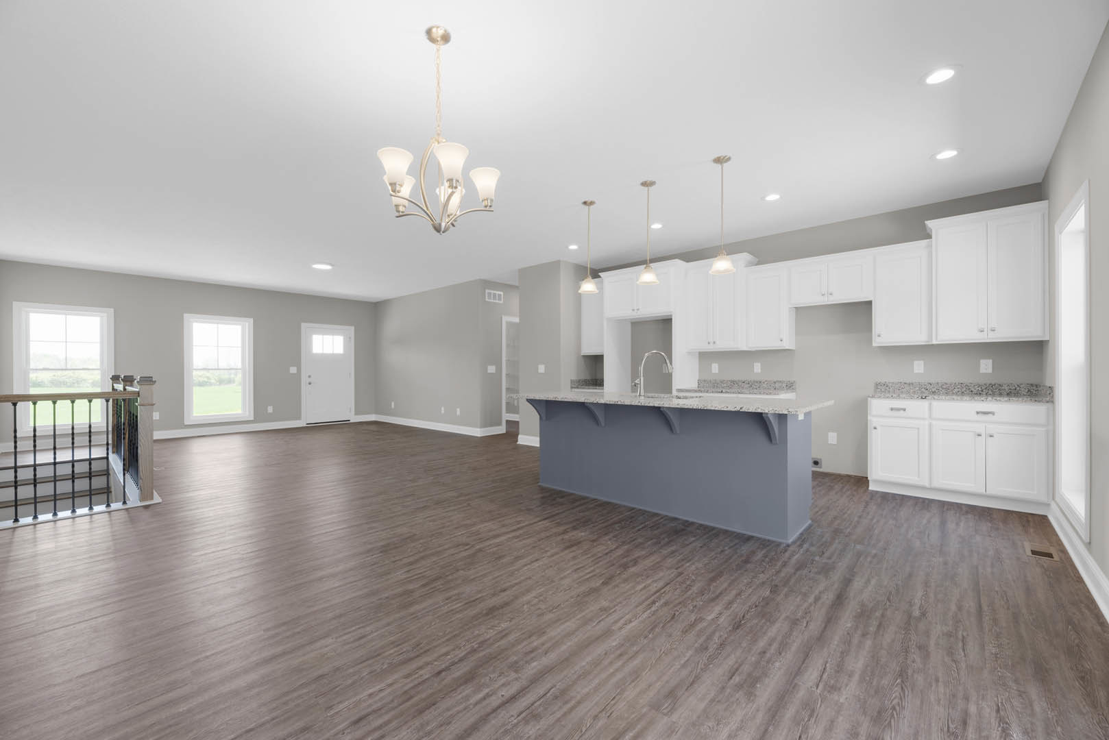 Open-concept kitchen and living room featuring hardwood floors, white cabinetry, stone countertop, stainless steel appliances, staircase with wood treads, large window overlooking