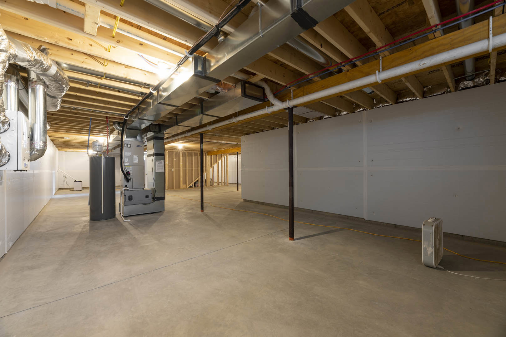 Exposed metal pipes and conduit on a plaster ceiling, concrete floor with yellow rope, white wall with additional piping, industrial finishes throughout