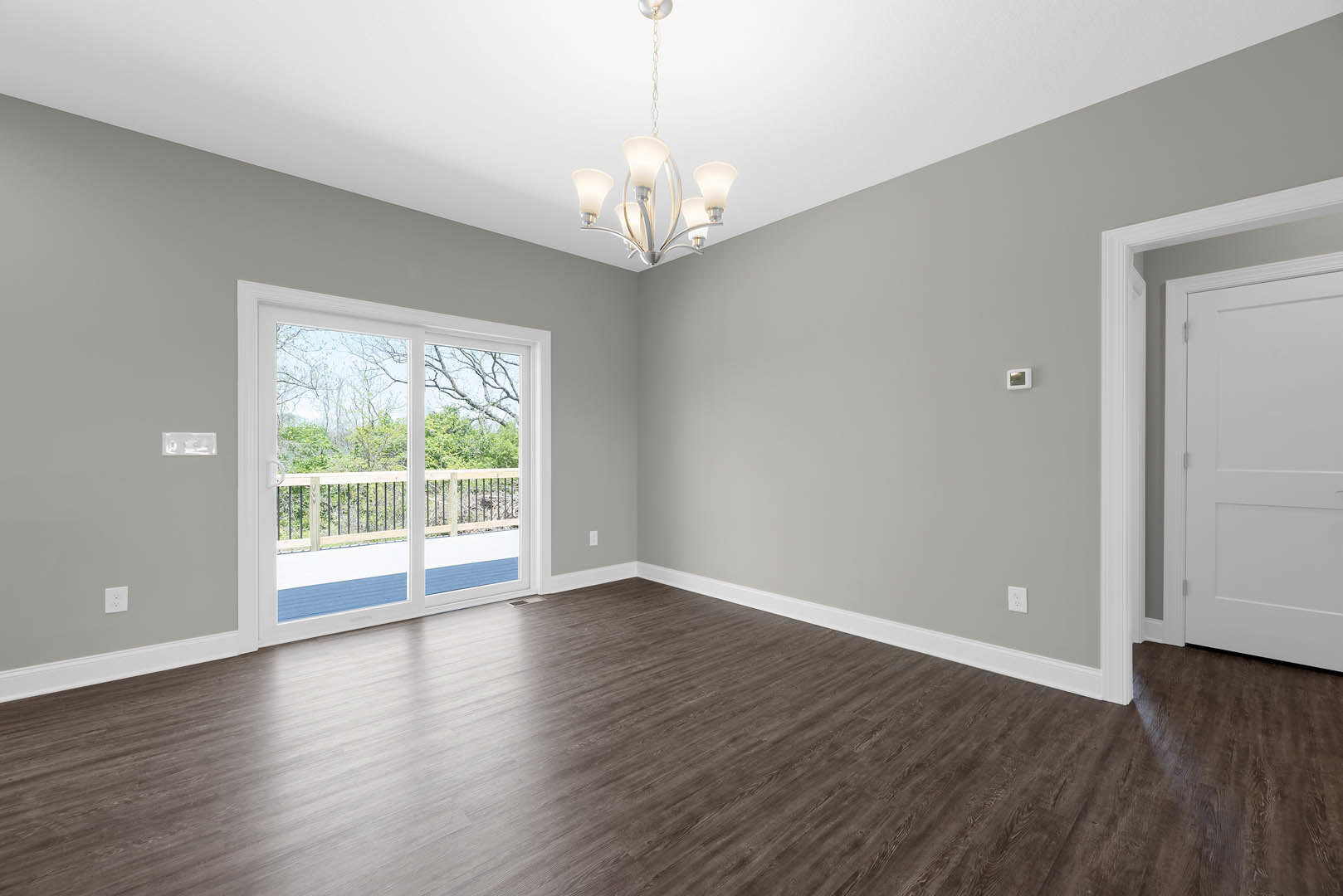 Wood flooring in a room with a white hinged door and a sliding glass door leading to a deck, five-light ceiling fixture, and close-up view of a metal railing