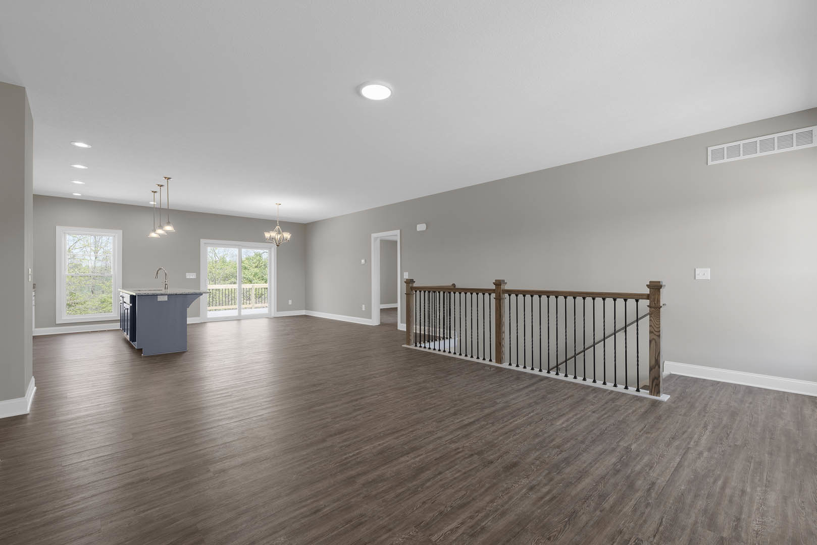 Spacious open-plan room featuring wood flooring, marble-topped kitchen island, ceiling light fixture, plaster walls, and large windows overlooking trees and outdoor scenery