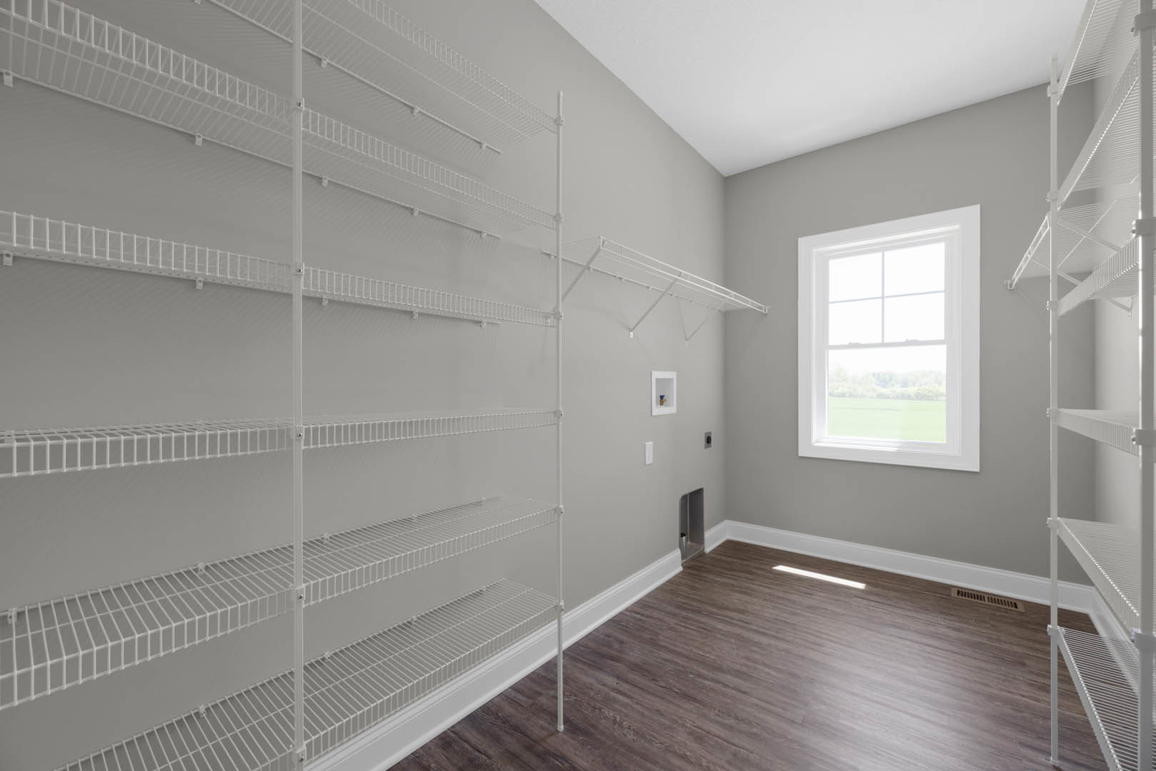 White built-in shelves along a plaster wall, wood flooring with white trim, large window overlooking a grassy field, natural light filling the room